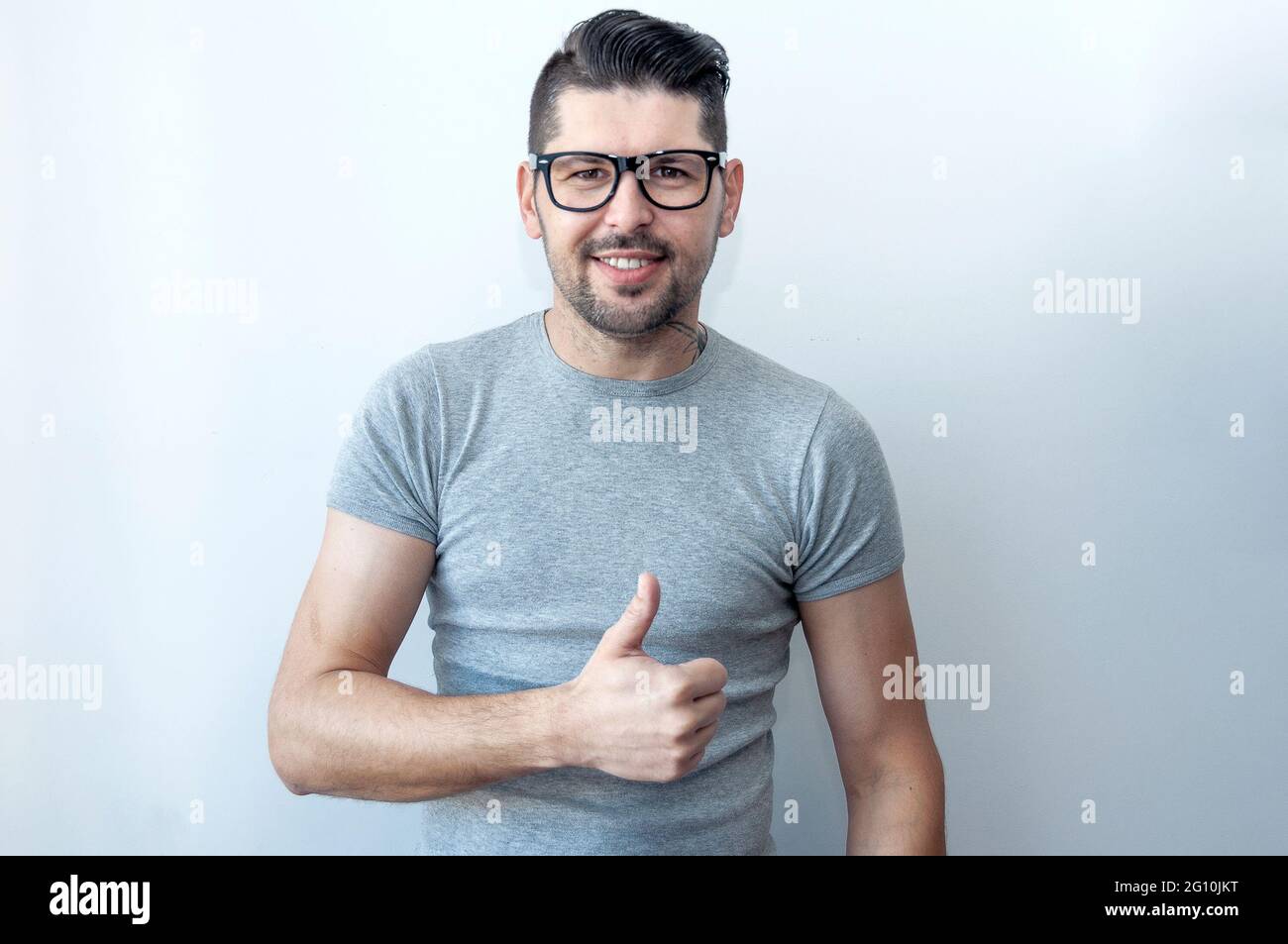 Joyeux jeune homme caucasien dans un t-shirt gris fait un pouce vers le haut signe montrant son soutien, respect et recommandé pour quelqu'un. Langue du corps. I l Banque D'Images