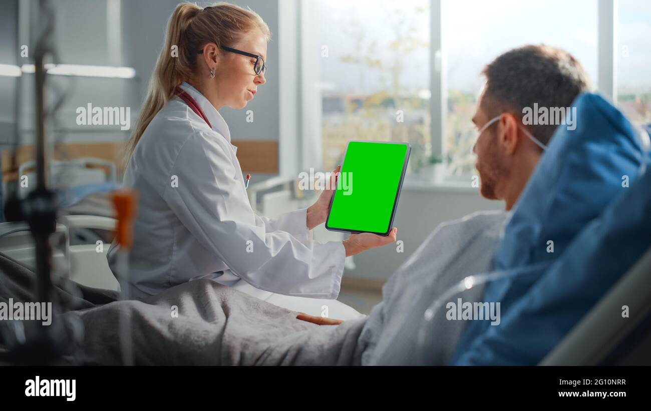Service hospitalier : une femme sympathique médecin parle à un patient malade qui se repose au lit, montre l'écran couleur vert tablette ordinateur, explique les résultats Banque D'Images