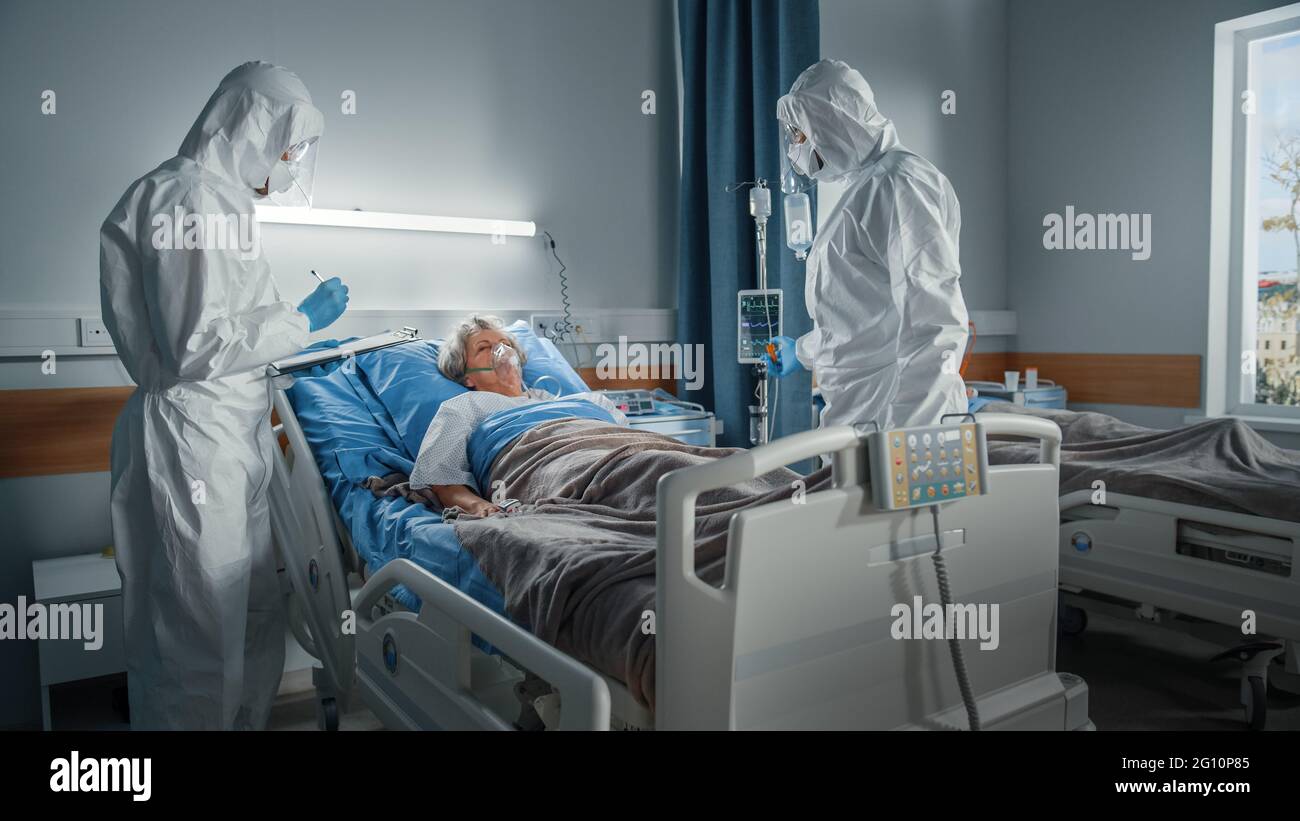 Hôpital coronavirus Service d'urgence quartier: Médecins, paramédics portant des combinaisons, masques de visage sauver la vie d'une femme senior couché dans le lit Banque D'Images