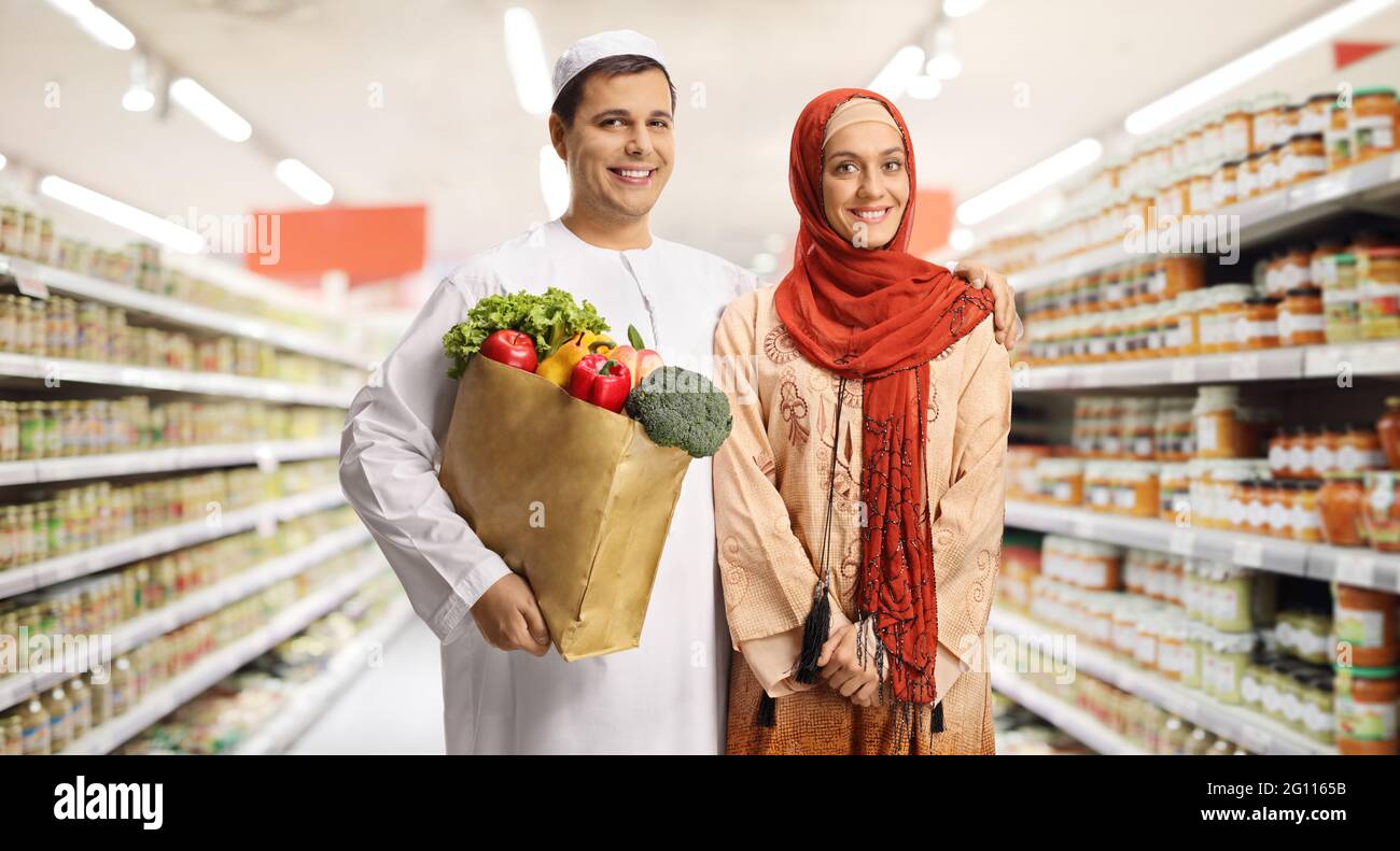 Un jeune couple musulman dans un supermarché tenant un sac de shopping en papier avec des provisions et posant Banque D'Images