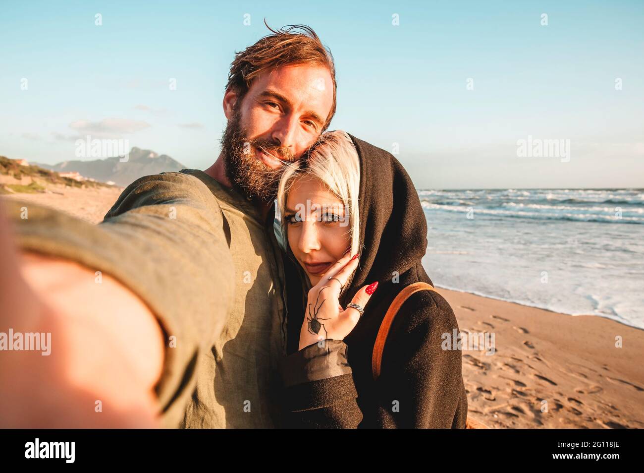 Couple de voyage amoureux de prendre selfie dans une plage déserte au coucher du soleil - femme avec regard magnétique et son petit ami de hipster s'amuser tout en regardant la came Banque D'Images