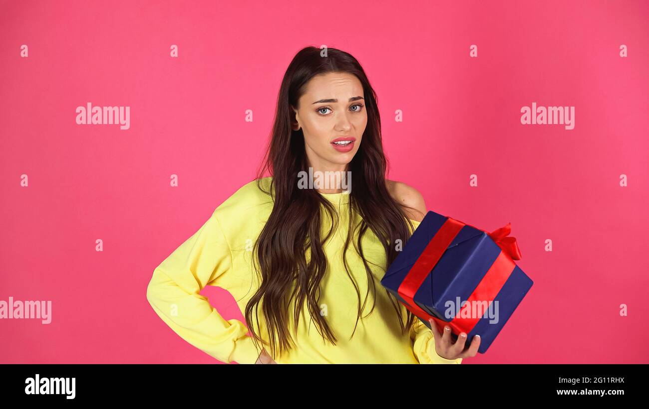 jeune femme adulte contrariée tenant une boîte cadeau à la main sur la posture de la hanche isolée sur le rose Banque D'Images