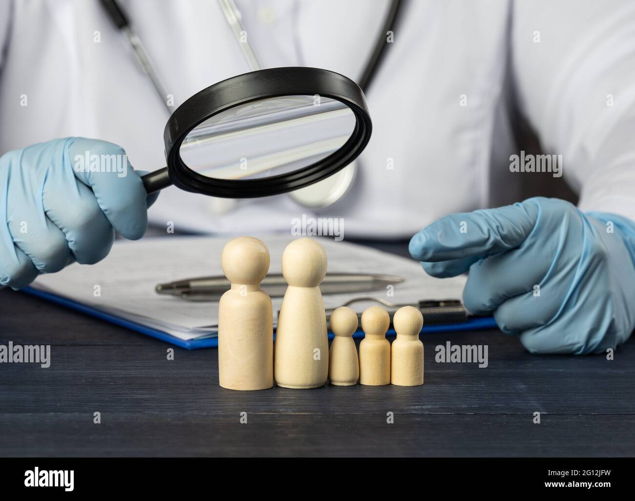 le médecin de famille tient une loupe sur une figurine en bois. Concept de recherche médicale, méthodes de traitement. La nécessité d'une assurance médicale. Banque D'Images