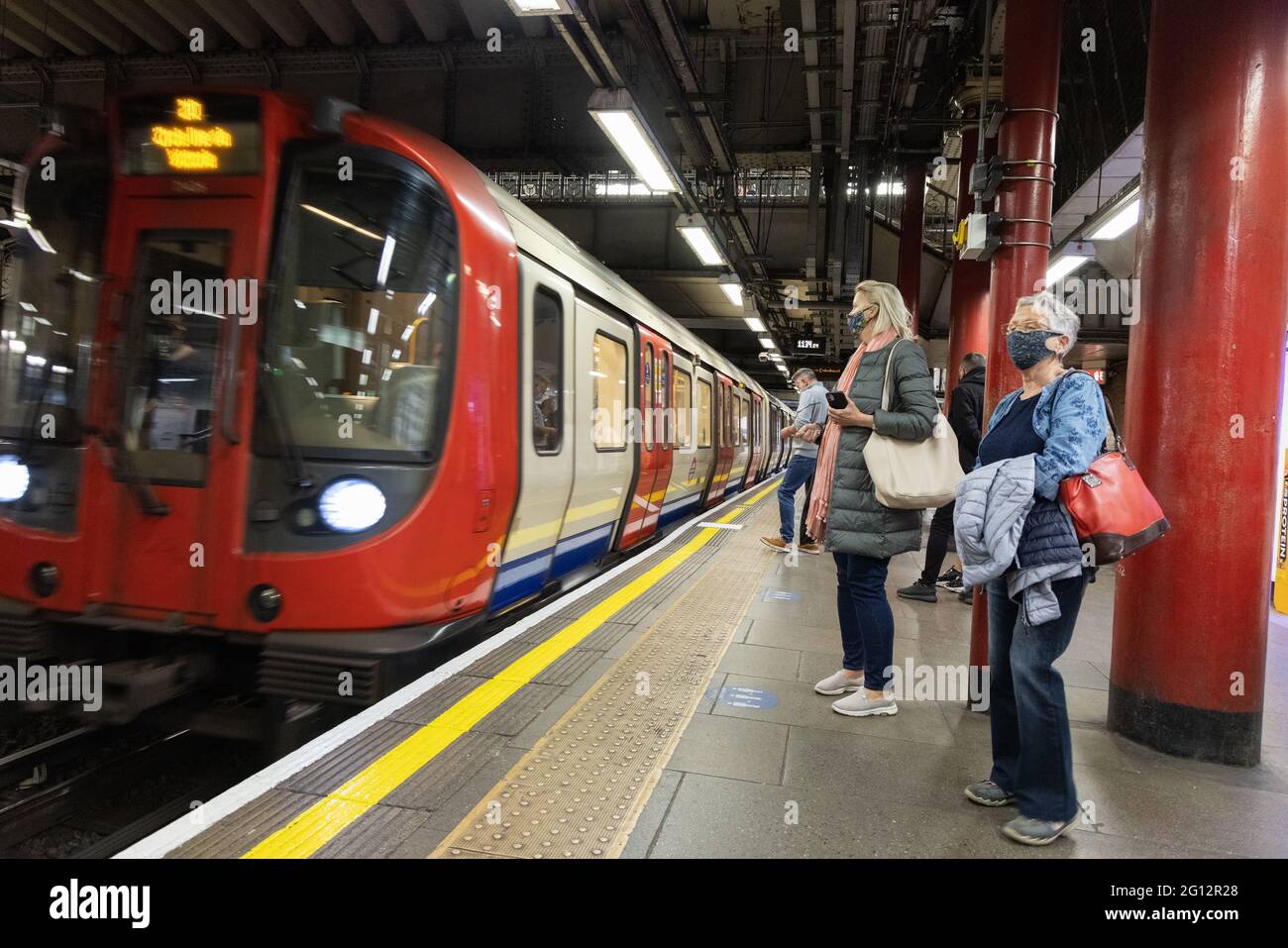Des personnes portant des masques et prenant des distances sociales sur la plate-forme lors de l'arrivée d'un train de métro, lors de la pandémie COVID 19, London Underground, Londres UK 2021 Banque D'Images