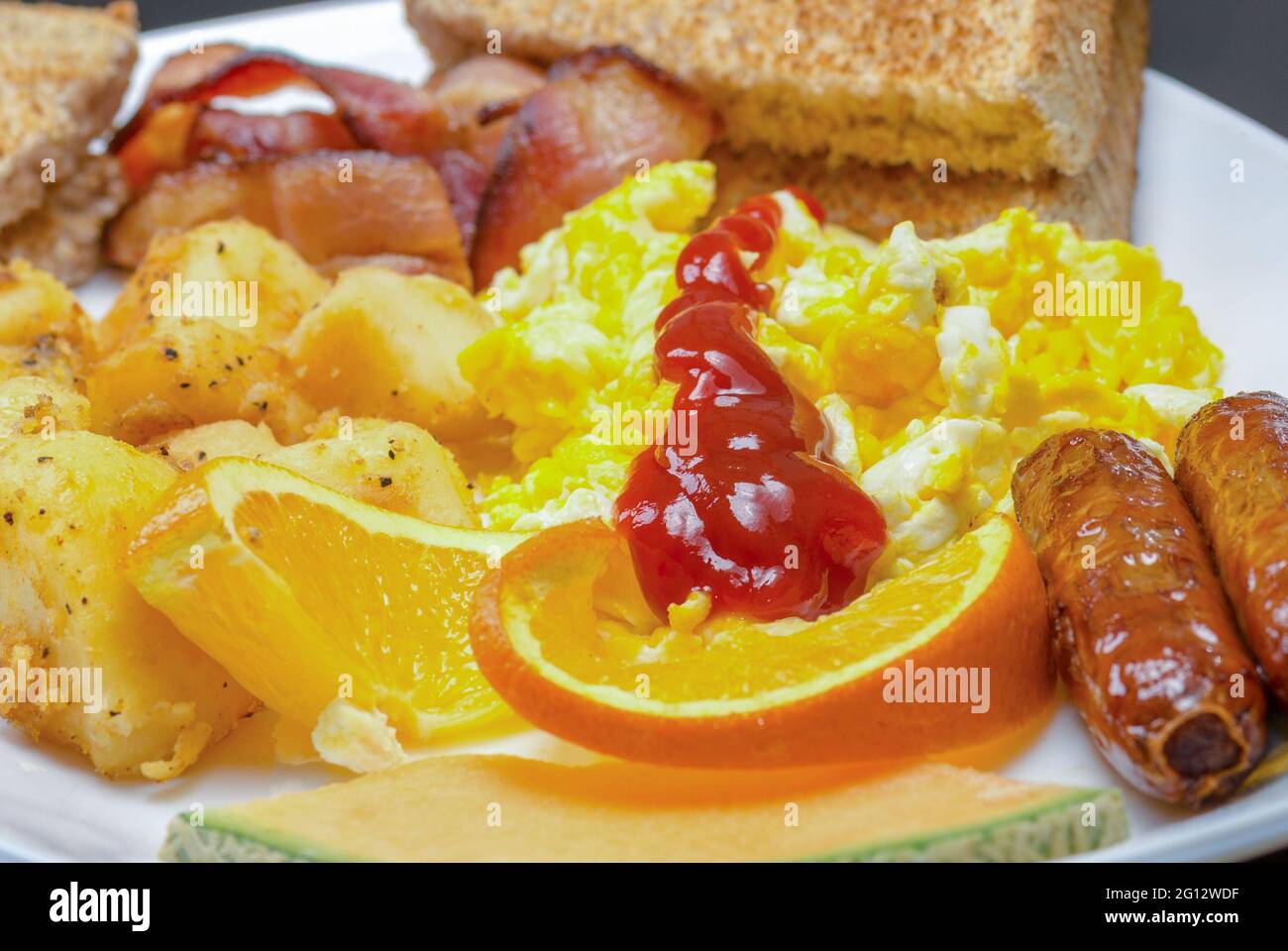 Plateau de petit-déjeuner. Œufs brouillés, pommes de terre du petit déjeuner, bacon, saucisses, toasts, tranches d'orange et de cantaloup Banque D'Images