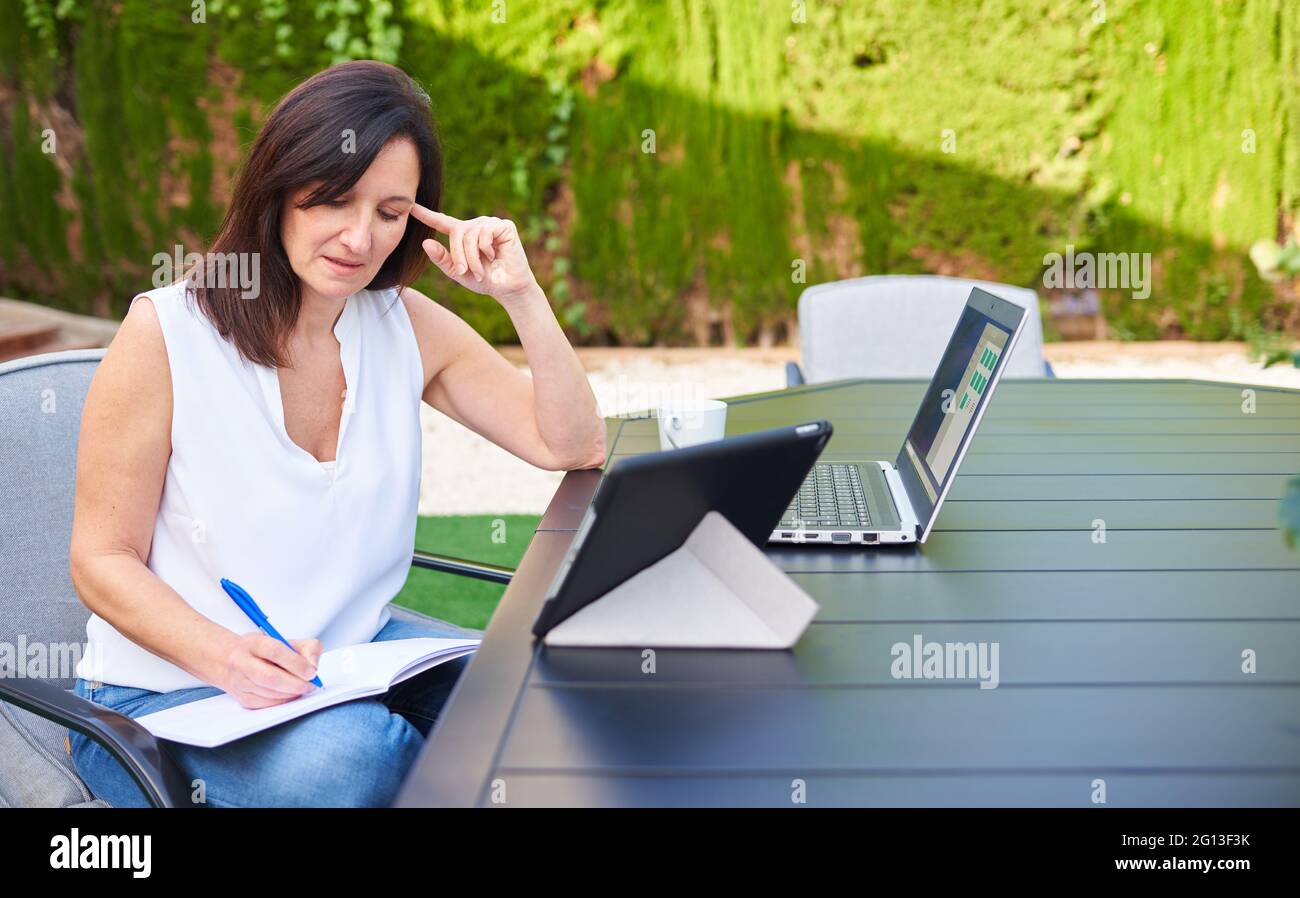 Une femme travaillant en télétravail lors d'une réunion d'affaires à l'extérieur tout en utilisant sa tablette pour ordinateur portable et en prenant des notes dans son ordinateur portable Banque D'Images