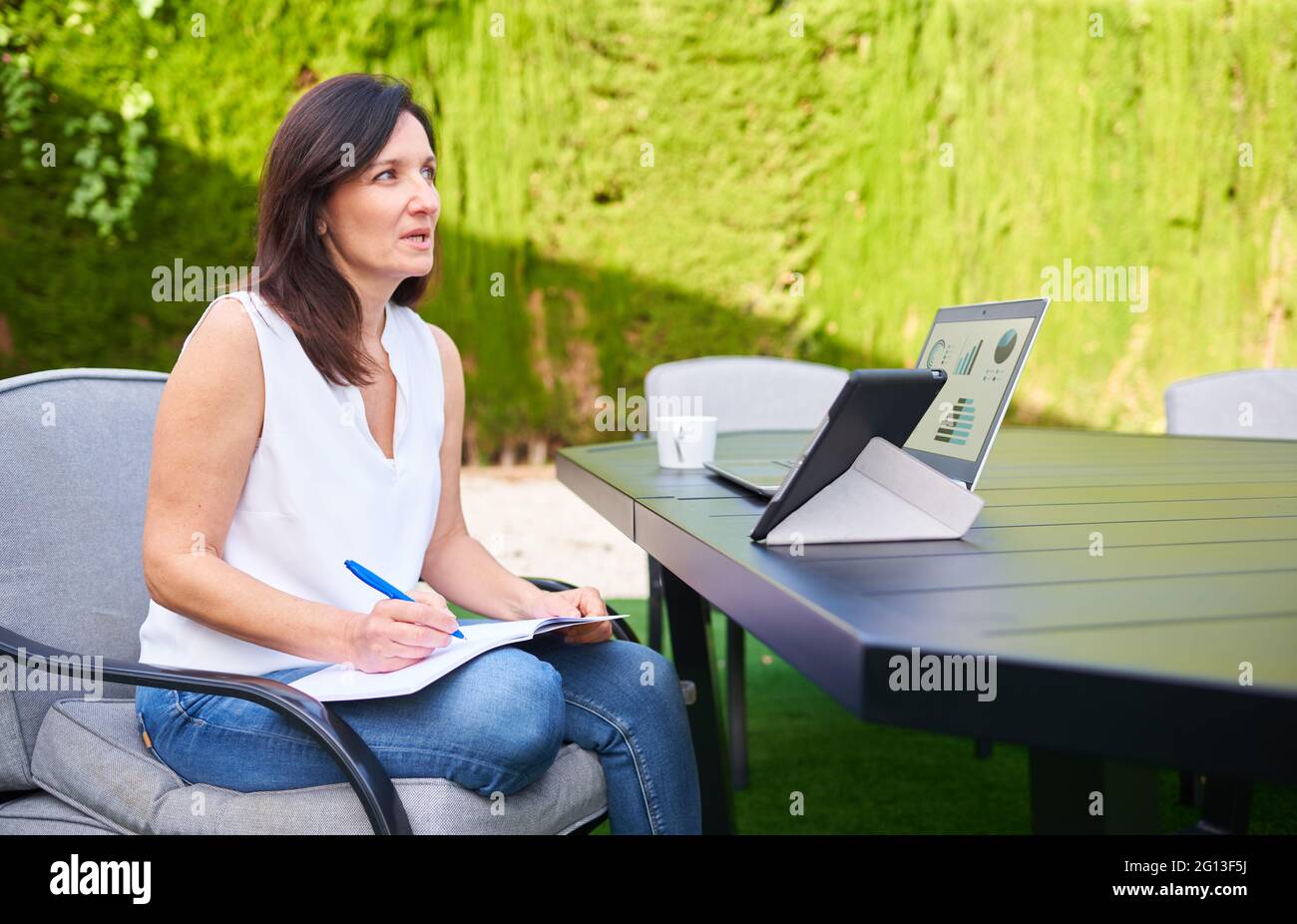 Une femme travaillant en télétravail lors d'une réunion d'affaires à l'extérieur tout en utilisant sa tablette pour ordinateur portable et en prenant des notes dans son ordinateur portable Banque D'Images