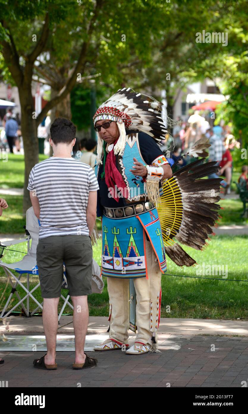 Un homme amérindien vêtu de la régalia indienne des plaines vend des œuvres d'art et parle avec les touristes sur la place historique de Santa Fe, au Nouveau-Mexique. Banque D'Images