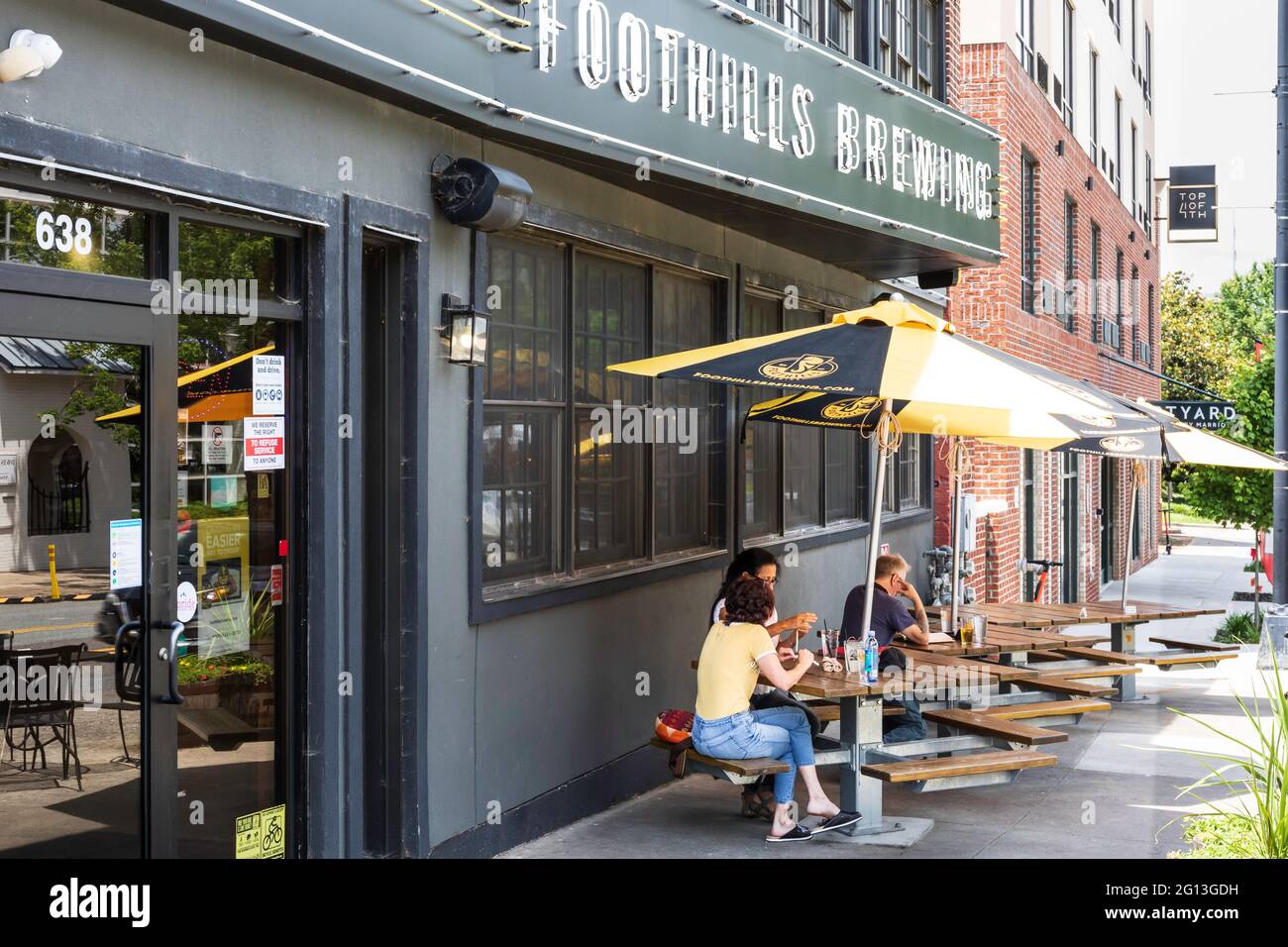 WINSTON-SALEM, NC, USA-1 JUIN 2021: 3 personnes s'assoient à des tables à l'extérieur de Foothills Brewing lors d'une chaude journée de printemps. Banque D'Images
