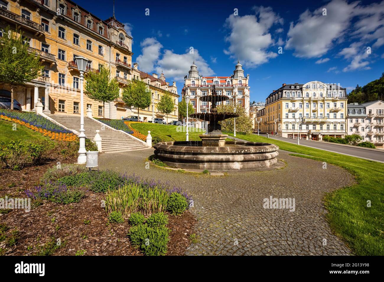 Marianske Lazne, République tchèque - Mai 30 2021 : la fontaine baroque se trouvant sur la place Goethe. Pelouse verte, fleurs et bâtiments de l'hôtel autour. Banque D'Images