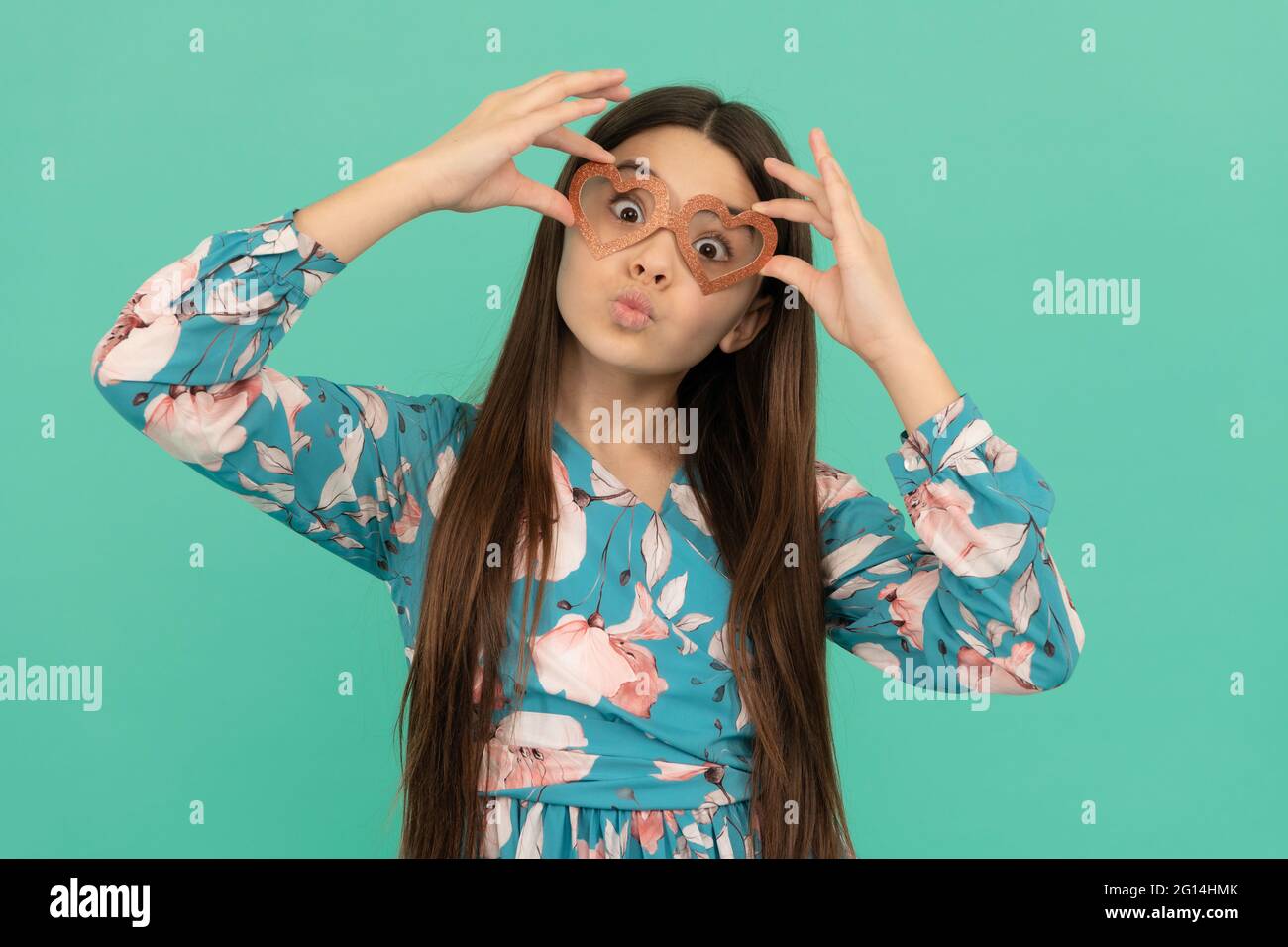 Drôle fille enfant avec baiser visage pout lèvres portant coeur-en forme de lunettes fond bleu, valentines Banque D'Images