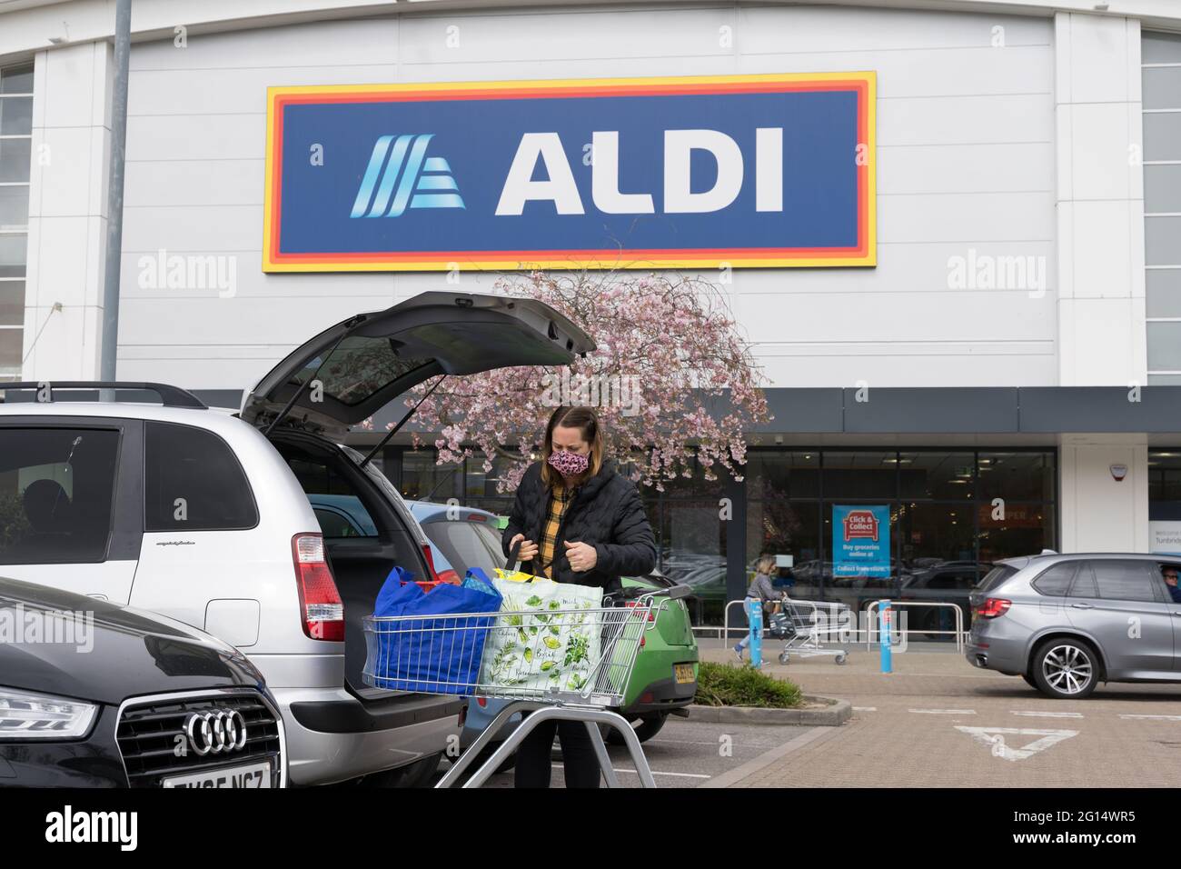 Une femme magasinant dans son coffre à l'extérieur du magasin Aldi, chaîne de supermarchés, Kent, Angleterre, Cherry Blossom à l'entrée du magasin Banque D'Images