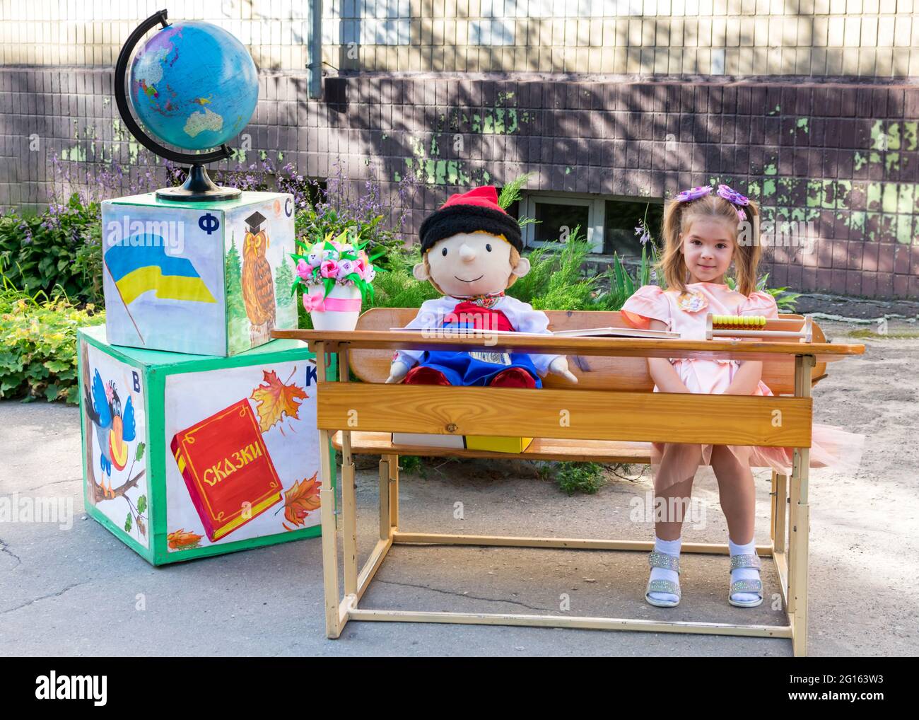 Lisichansk, Ukraine. 09.01.2020. Petite belle écolière s'assoit à un bureau avec une poupée jouet d'un garçon en vêtements nationaux ukrainiens sur le fond Banque D'Images