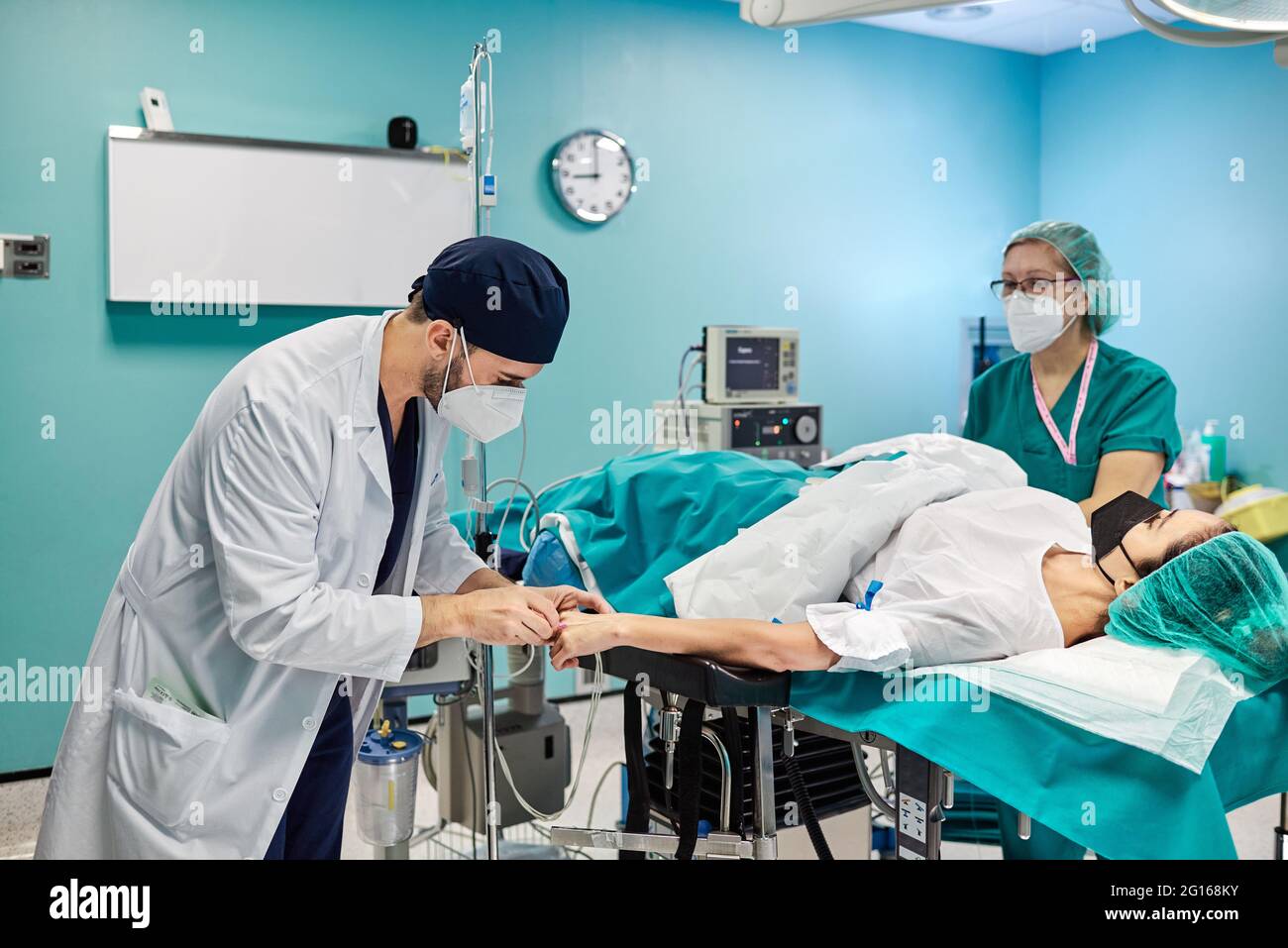 Médecin de sexe masculin avec un partenaire en uniforme médical préparant une patiente sous masque à oxygène pour une opération à l'hôpital Banque D'Images