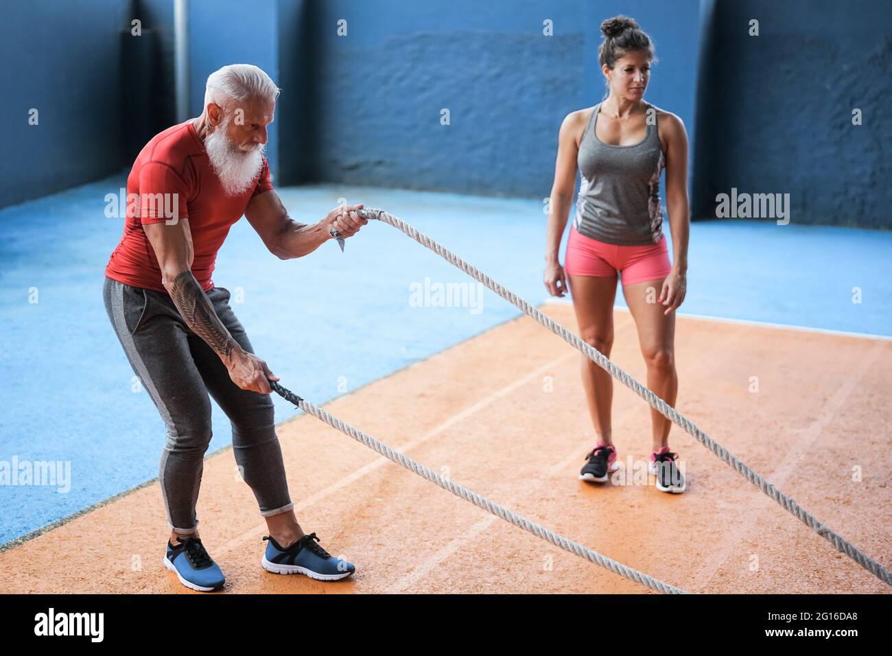 Entraînement d'homme senior avec exercice de corde de bataille dans la salle de gym - entraînement d'homme de forme mature dans le centre de club de bien-être - Sport concept de mode de vie sain Banque D'Images