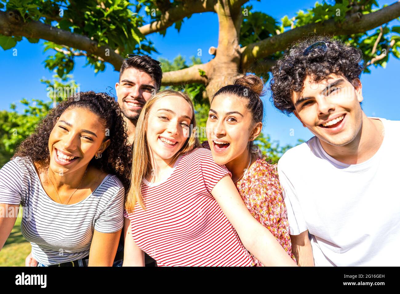 Groupe de cinq amis très heureux ayant l'amusement au parc posant regardant la caméra pour un portrait. Gen z multiracial insouciance jeunes femmes et hommes togeth Banque D'Images