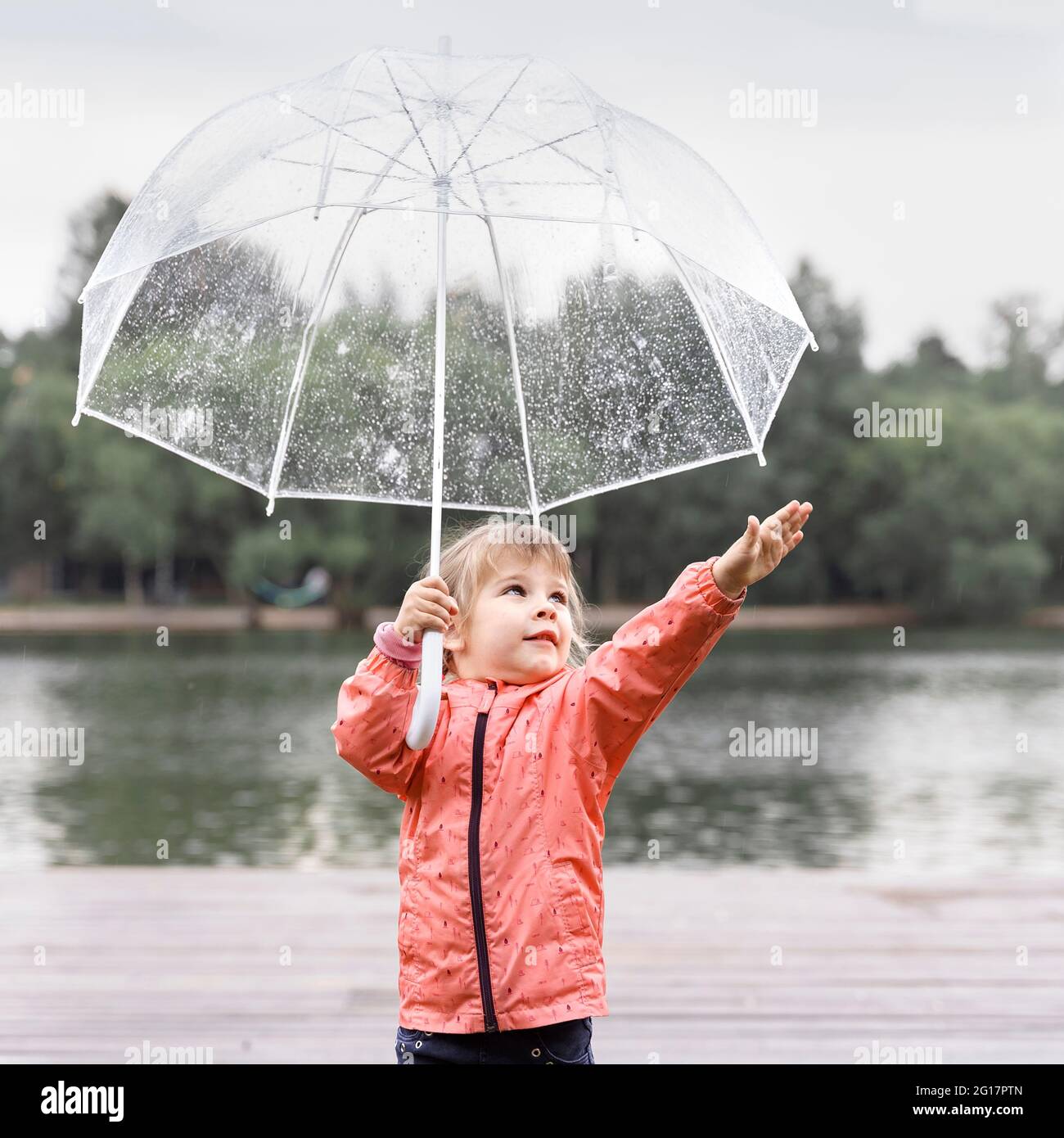 mignon caucasien fille d'enfant avec parapluie transparent ayant le plaisir dans la pluie Banque D'Images