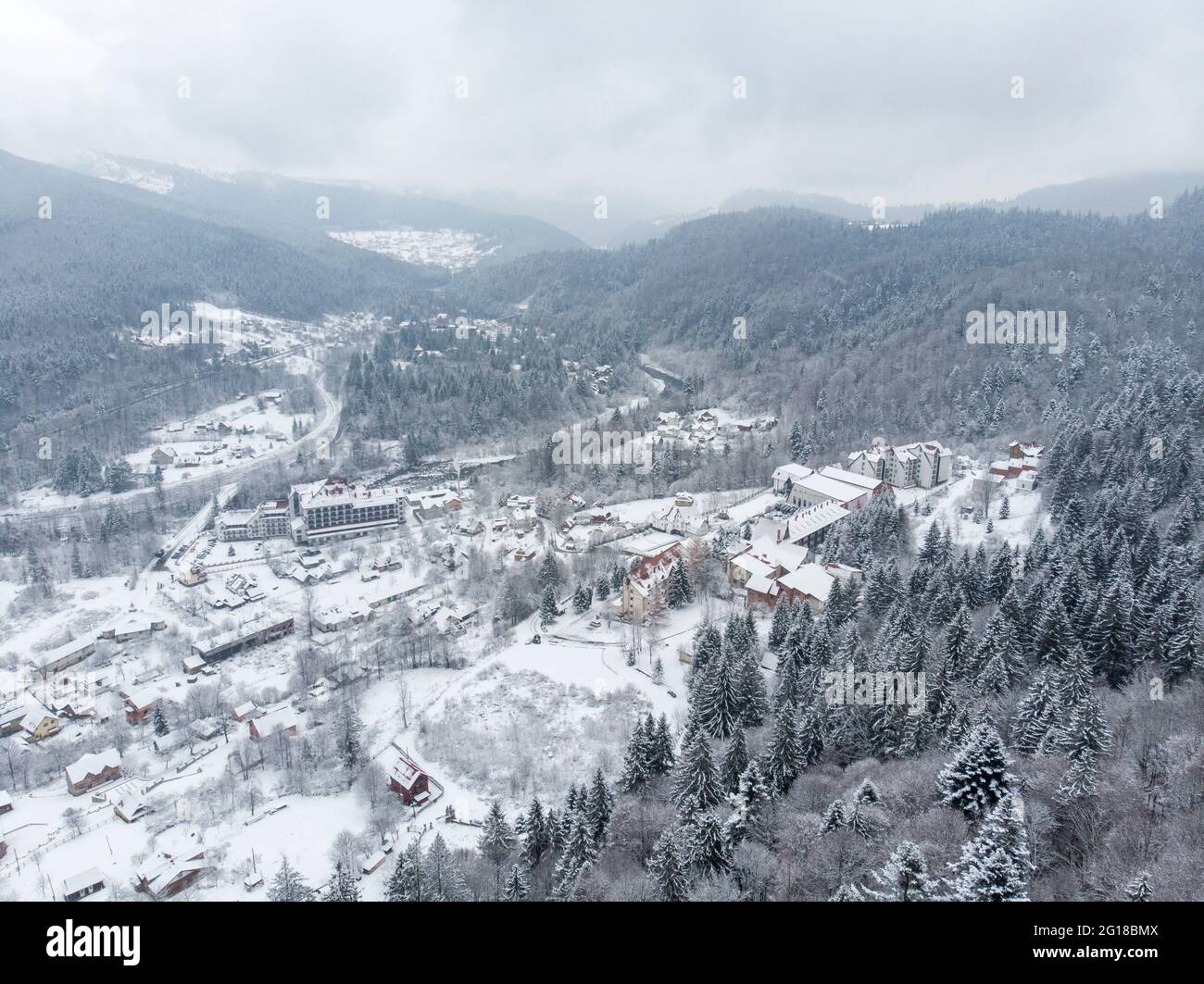 Vue aérienne d'un village de montagne avec des collines couvertes de neige et de forêt de pins en hiver. Yaremche, Ukraine. Survolant les collines enneigées et le bois Banque D'Images