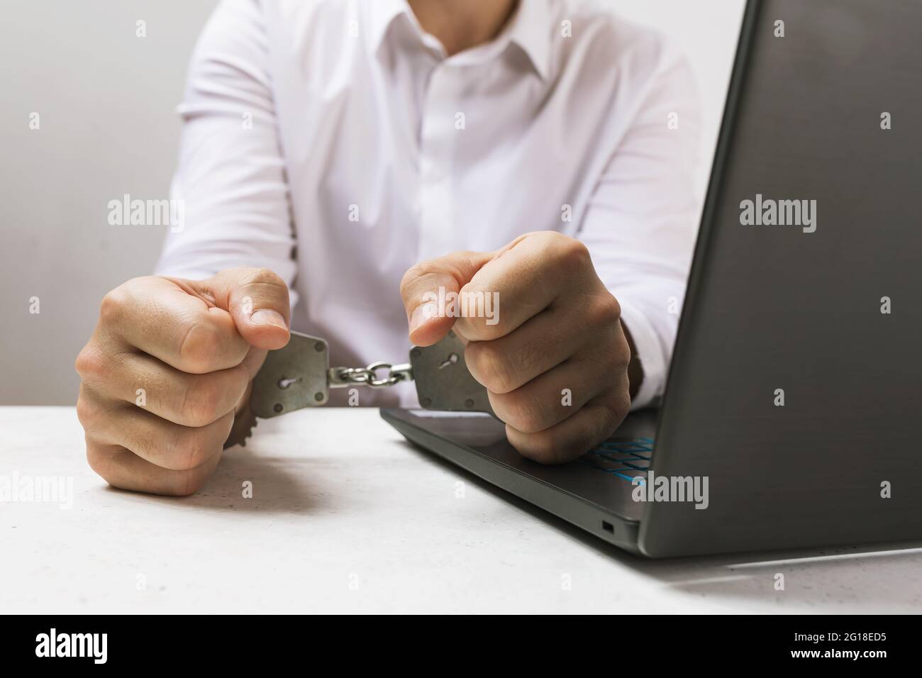 Un homme aux menottes près d'un ordinateur portable, un concept sur le thème des crimes informatiques. Banque D'Images
