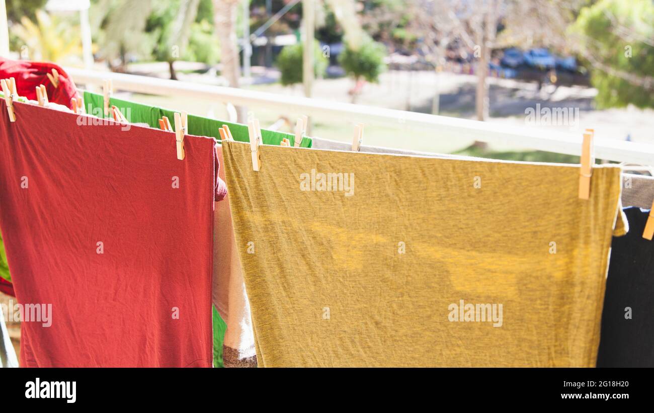 T-shirts colorés et autres vêtements étirés sur plusieurs cordes sur une terrasse exposée à l'air et au soleil pour sécher. Banque D'Images