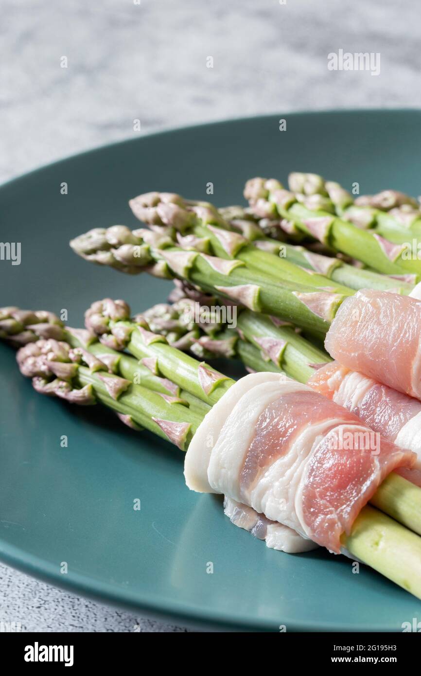 Asperges enrobées de bacon sur une assiette verte bleue. Avec un arrière-plan concret Banque D'Images