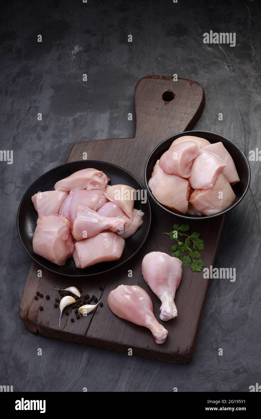 Ensemble de coupes de poulet cru, combinaison de coupes de curry de poulet sans peau, de coupes de poulet et de deux pilons disposés sur une planche en bois avec des feuilles de coriandre Banque D'Images