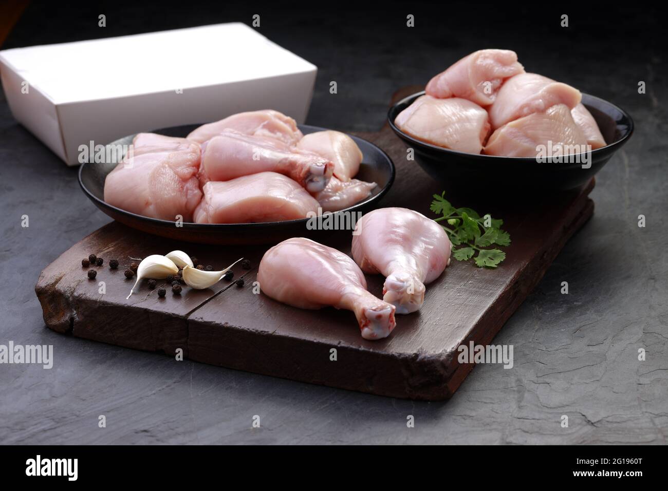 Ensemble de coupes de poulet cru, combinaison de coupes de curry de poulet sans peau, de coupes de poulet et de deux pilons disposés sur une planche en bois avec des feuilles de coriandre Banque D'Images