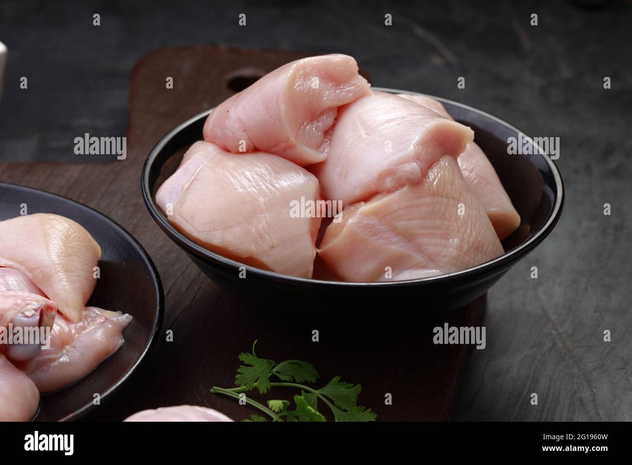 Ensemble de coupes de poulet cru, combinaison de coupes de curry de poulet sans peau, de coupes de poulet et de deux pilons disposés sur une planche en bois avec des feuilles de coriandre Banque D'Images