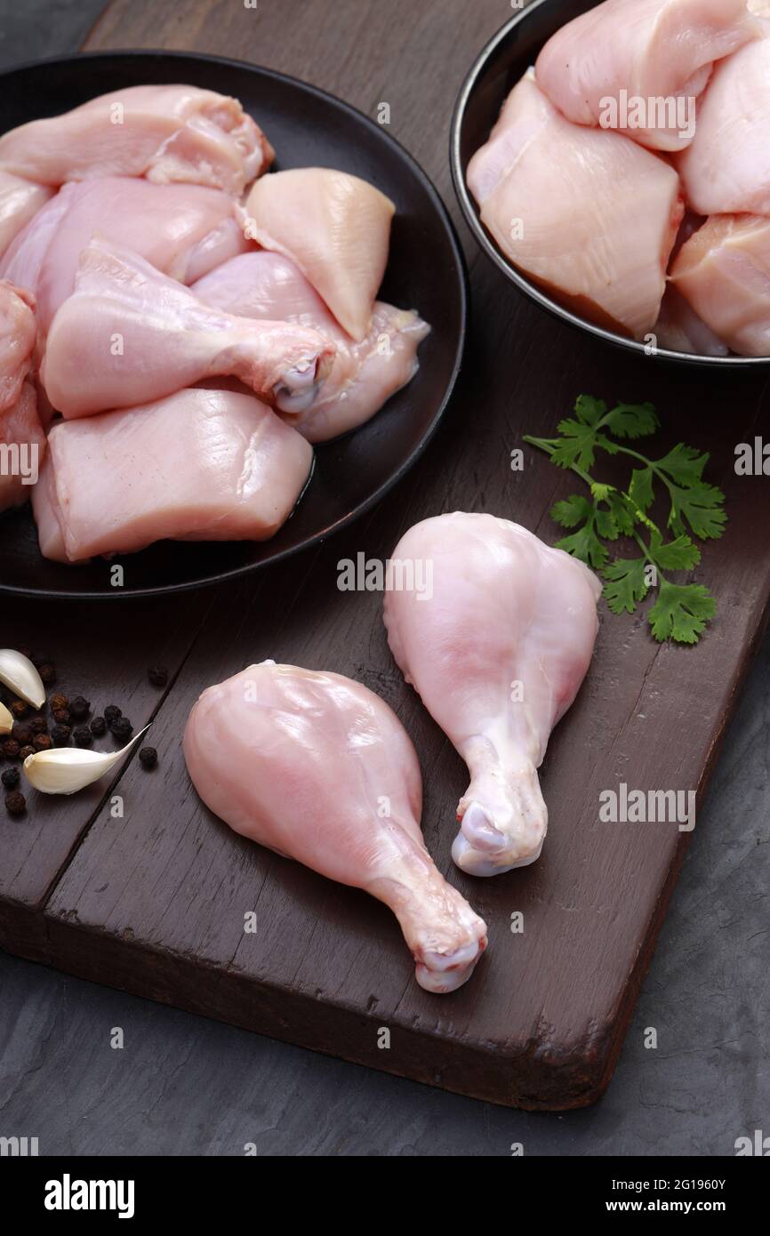 Ensemble de coupes de poulet cru, combinaison de coupes de curry de poulet sans peau, de coupes de poulet et de deux pilons disposés sur une planche en bois avec des feuilles de coriandre Banque D'Images