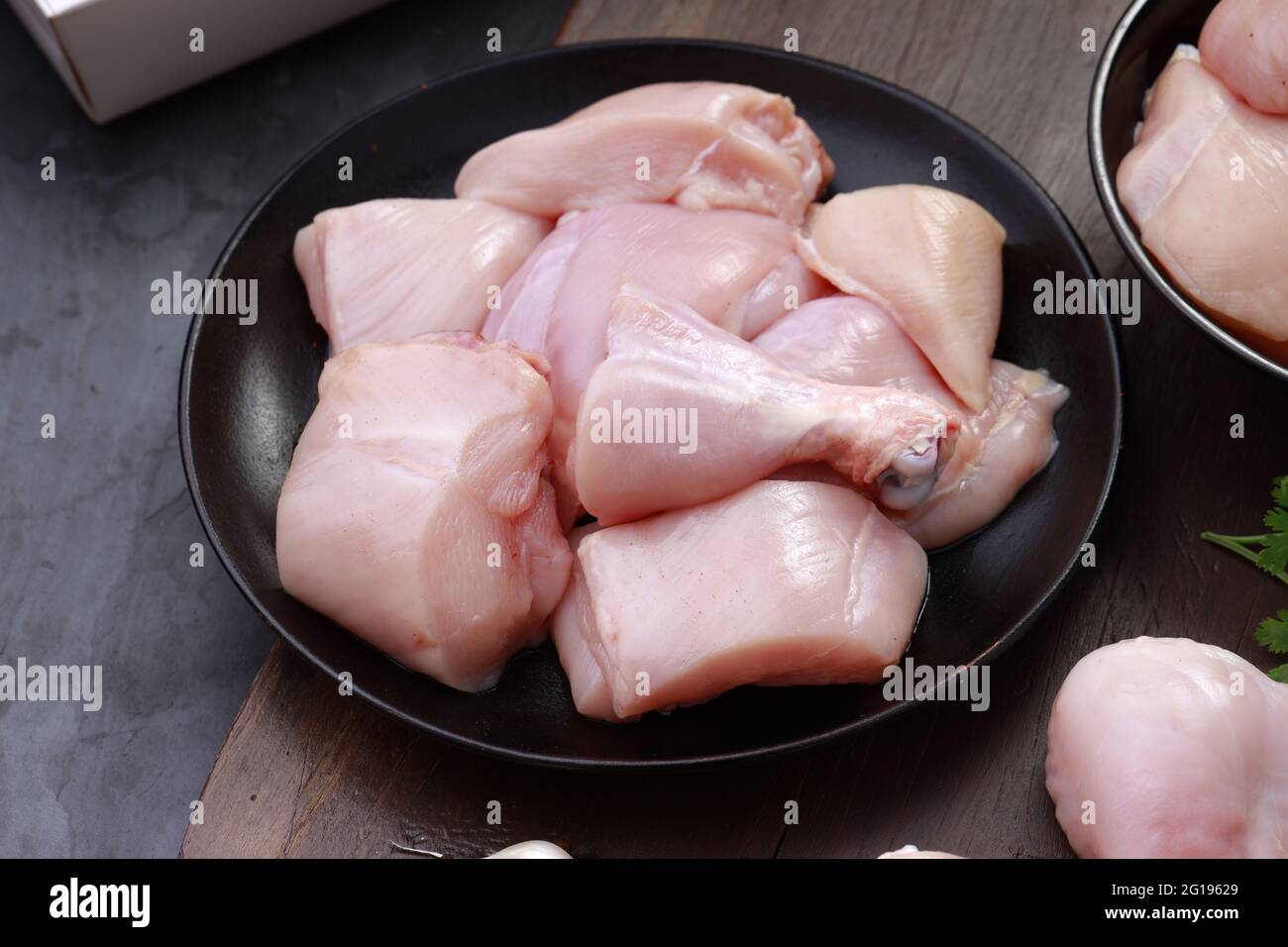 Ensemble de coupes de poulet cru, combinaison de coupes de curry de poulet sans peau, de coupes de poulet et de deux pilons disposés sur une planche en bois avec des feuilles de coriandre Banque D'Images