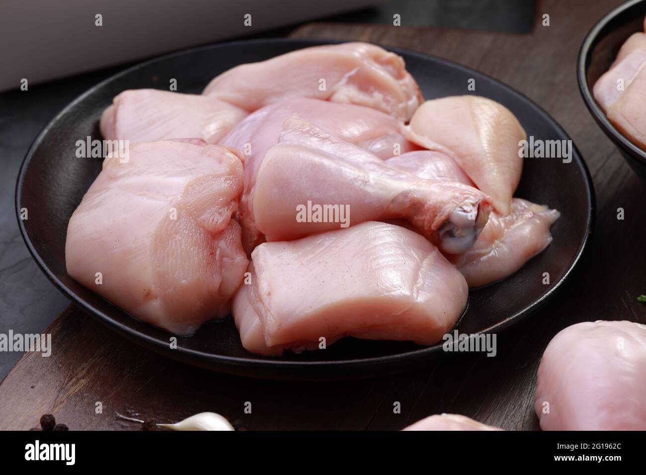 Ensemble de coupes de poulet cru, combinaison de coupes de curry de poulet sans peau, de coupes de poulet et de deux pilons disposés sur une planche en bois avec des feuilles de coriandre Banque D'Images