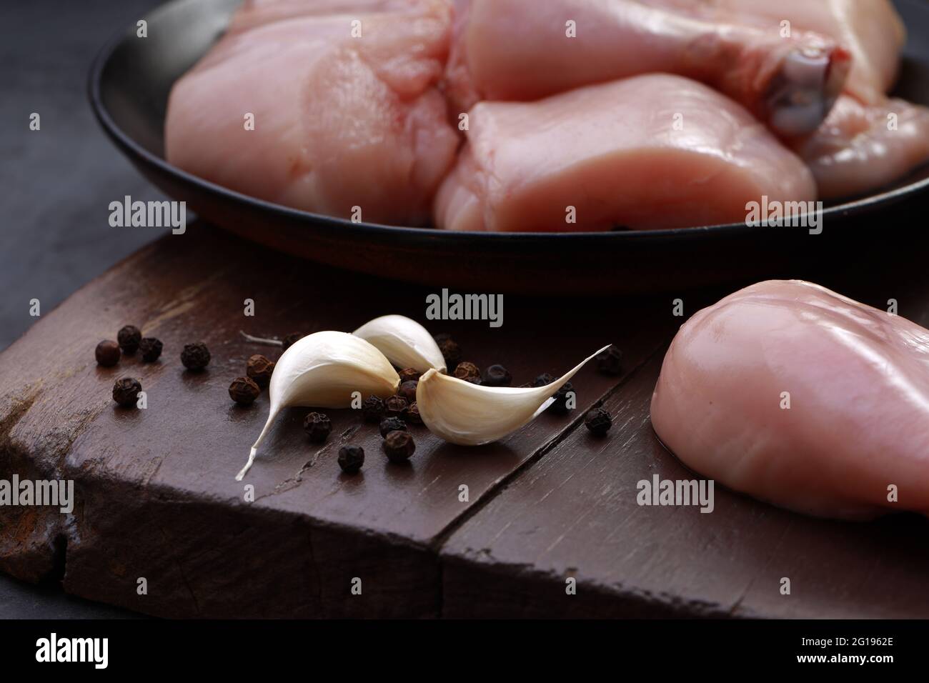 Ensemble de coupes de poulet cru, combinaison de coupes de curry de poulet sans peau, de coupes de poulet et de deux pilons disposés sur une planche en bois avec des feuilles de coriandre Banque D'Images