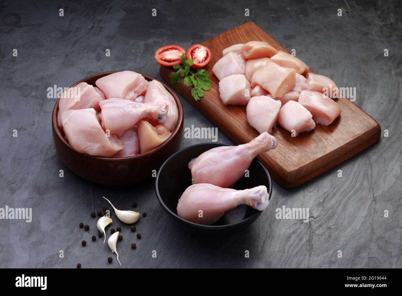 Ensemble de coupes de poulet cru, combinaison de coupes de curry de poulet sans peau, de coupes de poulet et de deux pilons disposés sur une planche en bois avec des feuilles de coriandre Banque D'Images