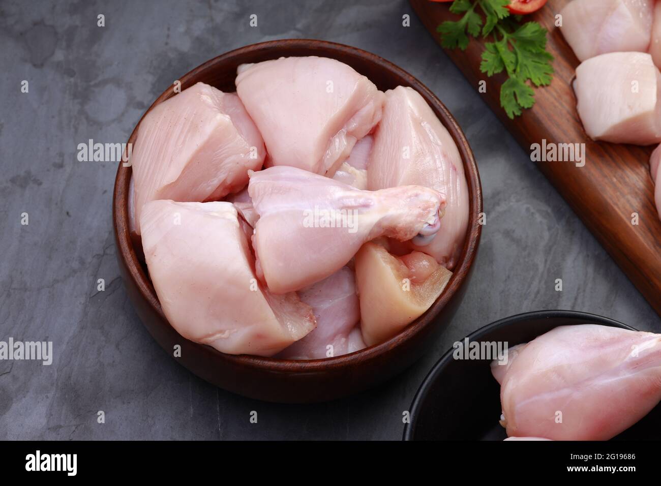 Ensemble de coupes de poulet cru, combinaison de coupes de curry de poulet sans peau, de coupes de poulet et de deux pilons disposés sur une planche en bois avec des feuilles de coriandre Banque D'Images