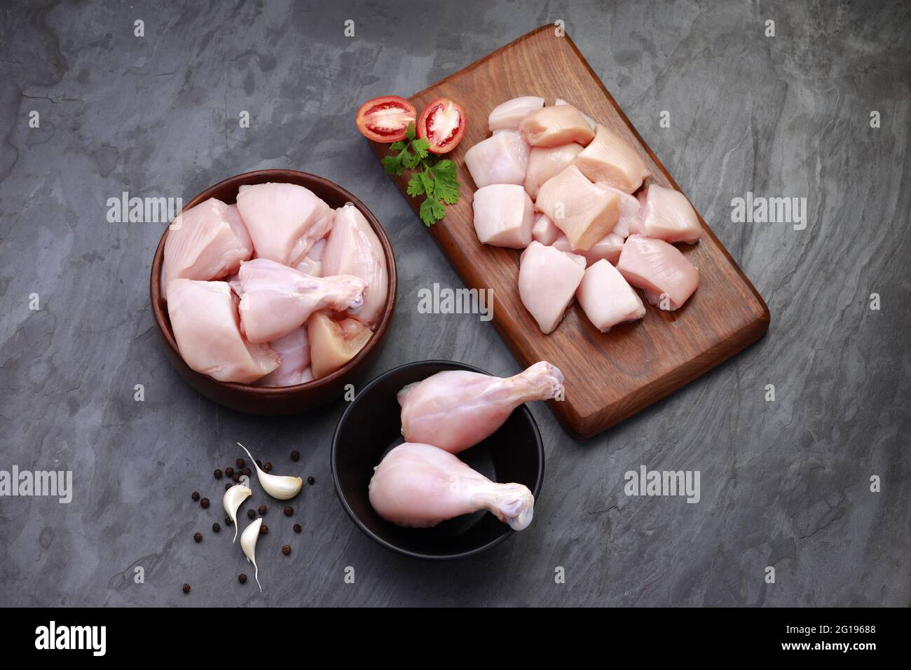 Ensemble de coupes de poulet cru, combinaison de coupes de curry de poulet sans peau, de coupes de poulet et de deux pilons disposés sur une planche en bois avec des feuilles de coriandre Banque D'Images