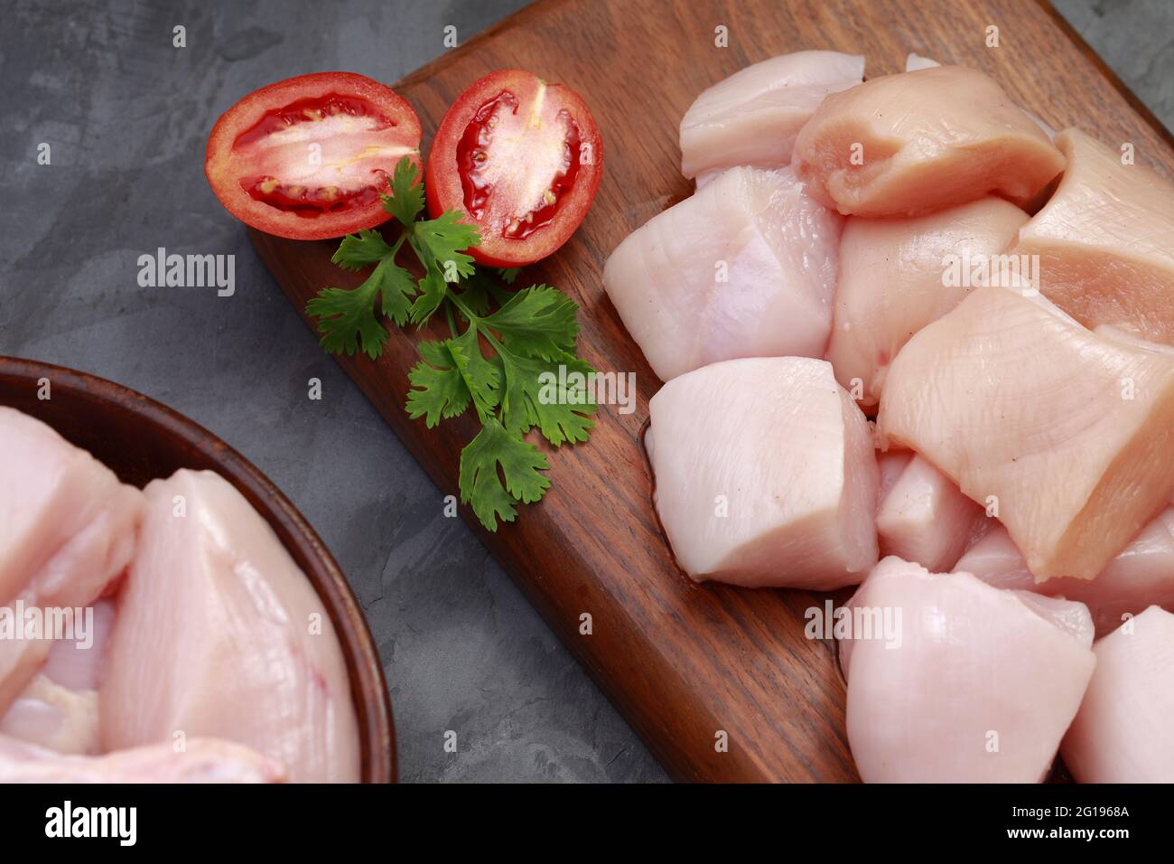 Ensemble de coupes de poulet cru, combinaison de coupes de curry de poulet sans peau, de coupes de poulet et de deux pilons disposés sur une planche en bois avec des feuilles de coriandre Banque D'Images