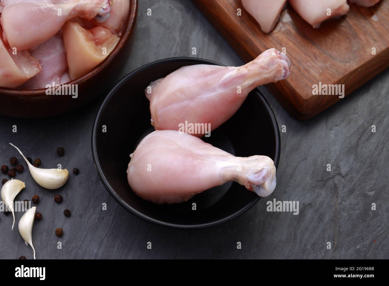 Ensemble de coupes de poulet cru, combinaison de coupes de curry de poulet sans peau, de coupes de poulet et de deux pilons disposés sur une planche en bois avec des feuilles de coriandre Banque D'Images