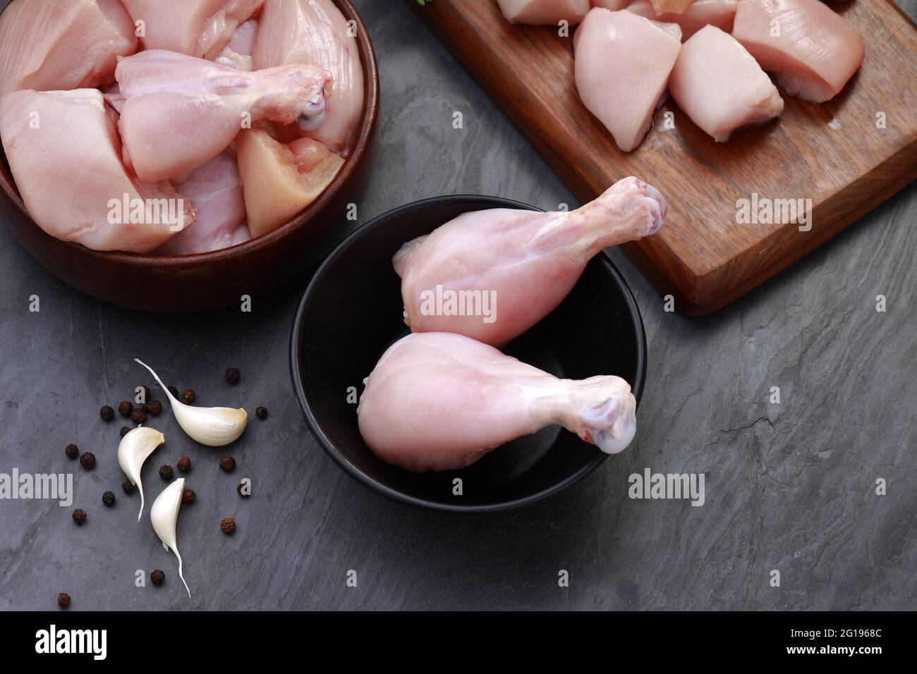 Ensemble de coupes de poulet cru, combinaison de coupes de curry de poulet sans peau, de coupes de poulet et de deux pilons disposés sur une planche en bois avec des feuilles de coriandre Banque D'Images