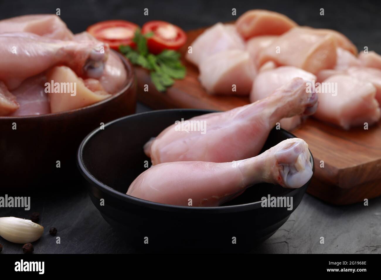 Ensemble de coupes de poulet cru, combinaison de coupes de curry de poulet sans peau, de coupes de poulet et de deux pilons disposés sur une planche en bois avec des feuilles de coriandre Banque D'Images