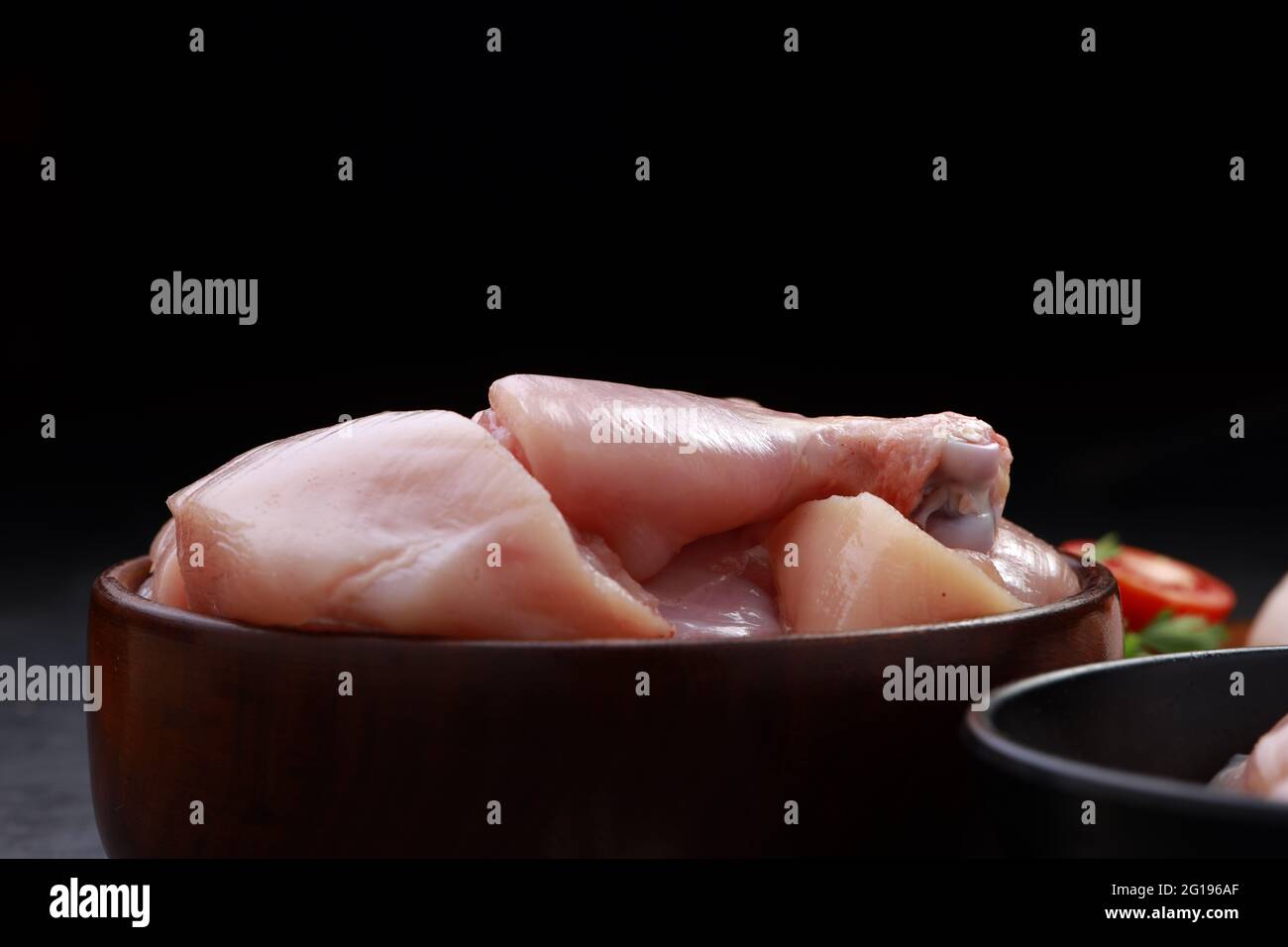 Ensemble de coupes de poulet cru, combinaison de coupes de curry de poulet sans peau, de coupes de poulet et de deux pilons disposés sur une planche en bois avec des feuilles de coriandre Banque D'Images