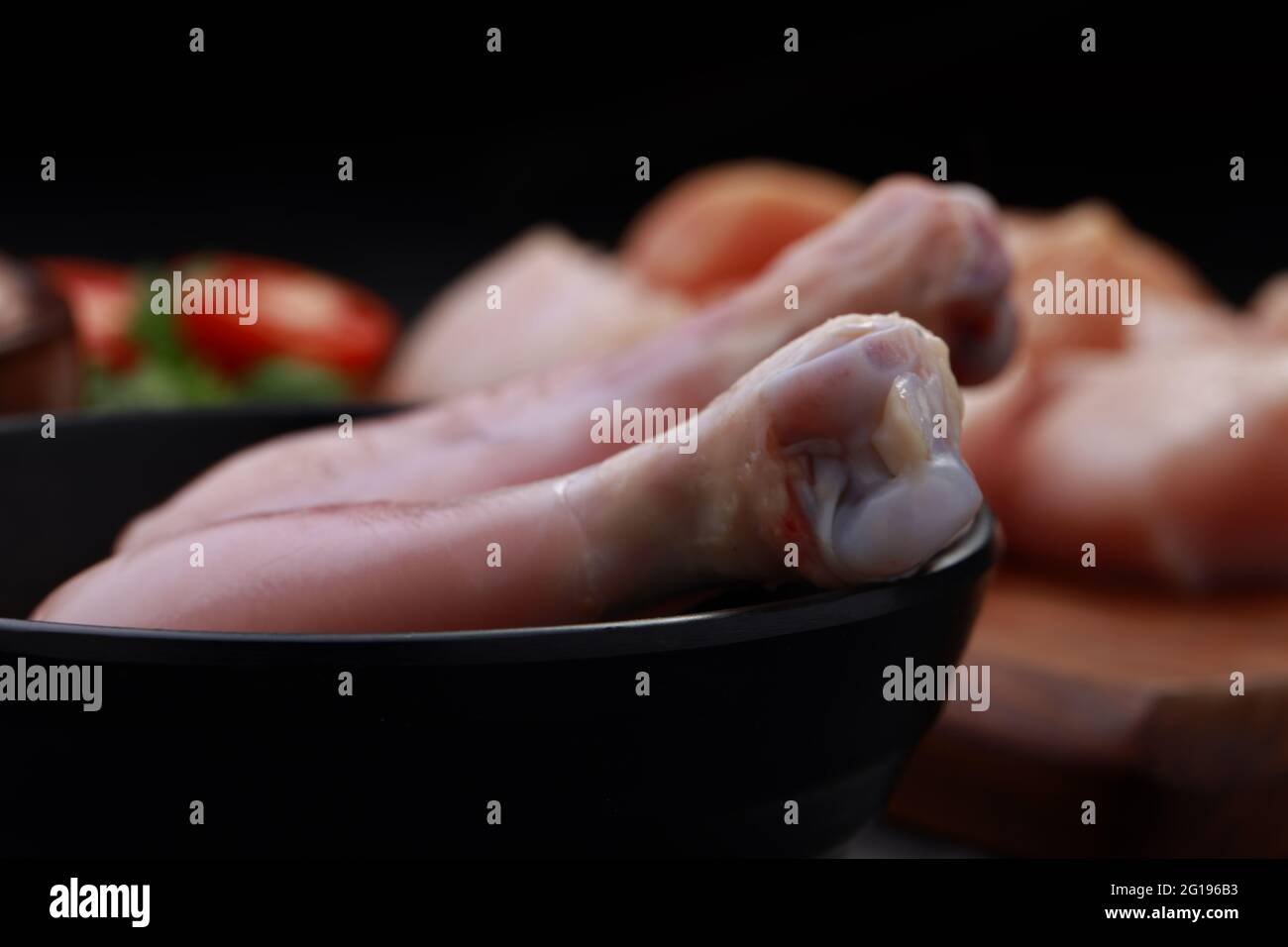 Ensemble de coupes de poulet cru, combinaison de coupes de curry de poulet sans peau, de coupes de poulet et de deux pilons disposés sur une planche en bois avec des feuilles de coriandre Banque D'Images