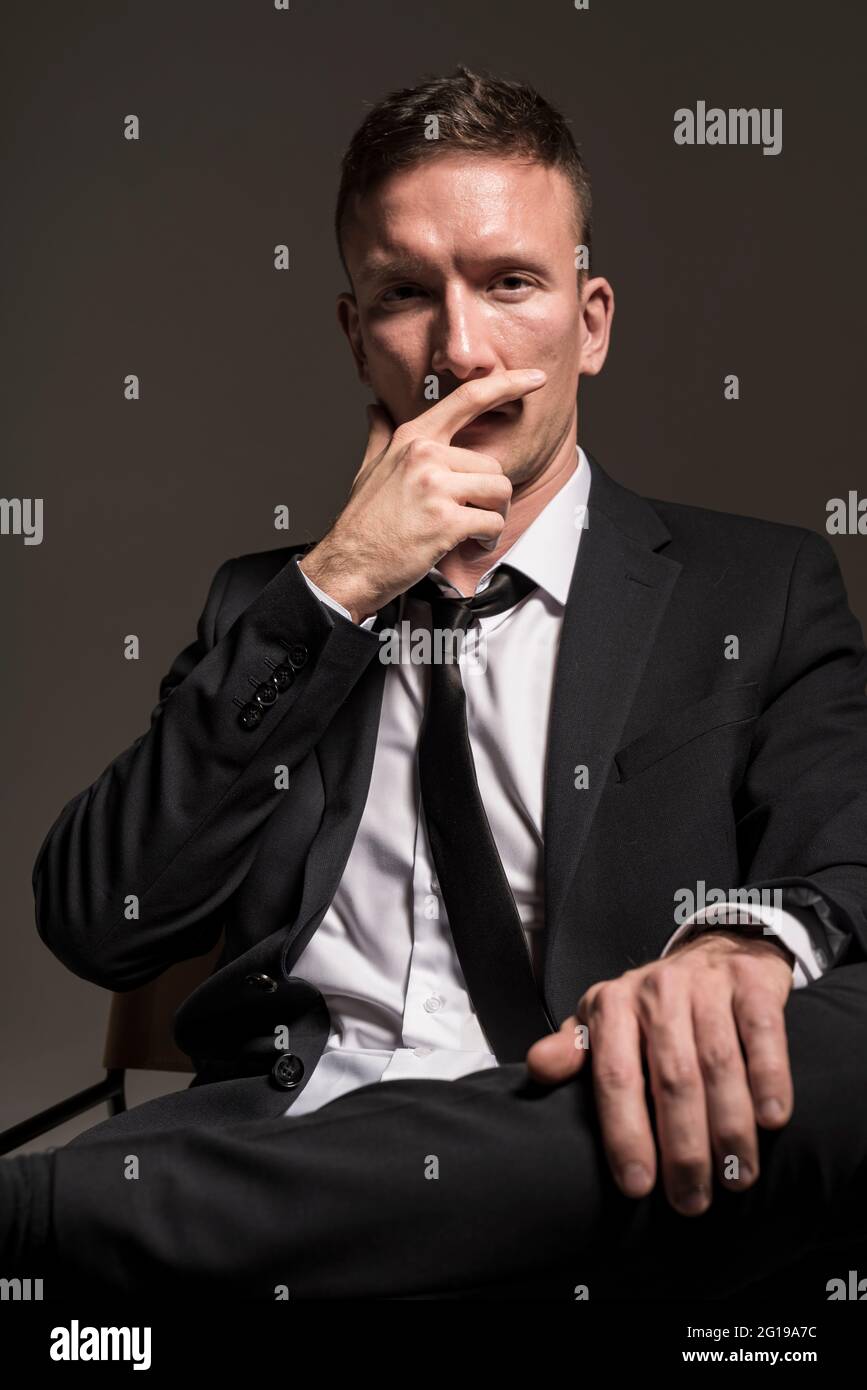 Portrait d'un homme confiant et pensif, dans un costume d'affaires, assis à pattes croisées sur un fond sombre. Banque D'Images