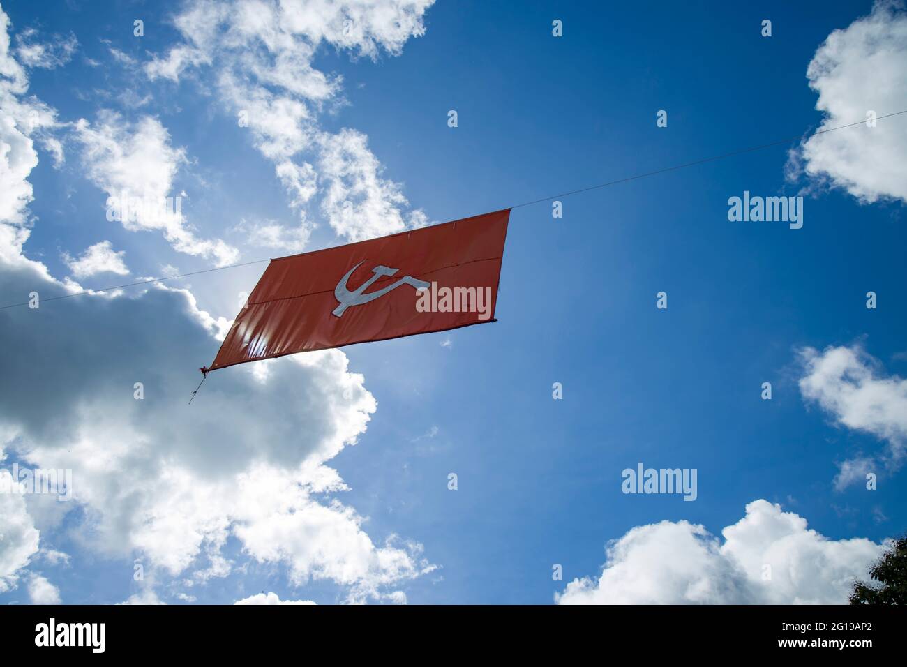 drapeau communiste. Marteau et faucille représentant les paysans et les ouvriers, volant dans l'épais ciel bleu ciel nuageux. Banque D'Images