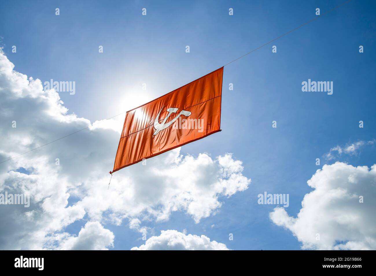 drapeau communiste. Marteau et faucille représentant les paysans et les ouvriers, volant dans l'épais ciel bleu ciel nuageux. Banque D'Images