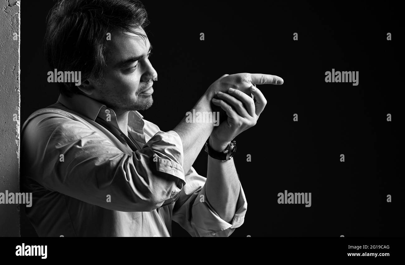 Portrait noir et blanc de l'homme adulte en chemise debout à l'arrière du mur de béton blanc tenant le doigt avec la main, visée Banque D'Images
