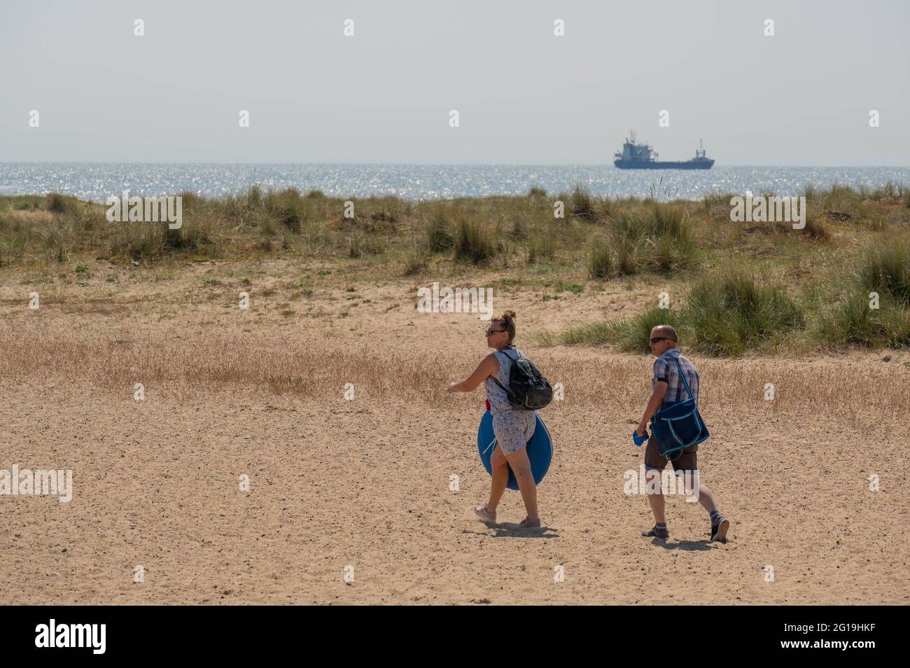 Les vacanciers qui marchent sur le sable vers la mer avec des sacs au soleil chauffent Banque D'Images