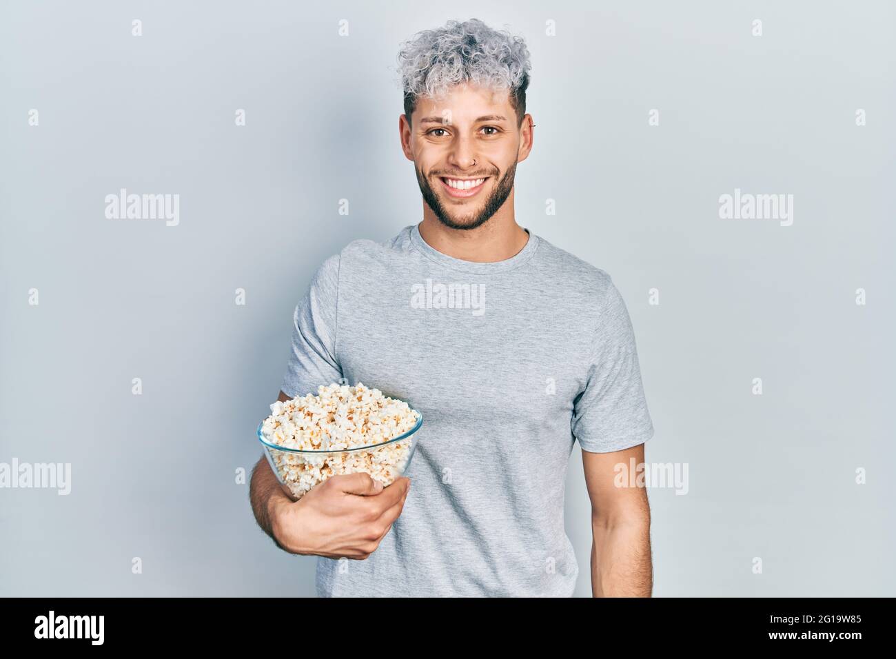 Jeune homme hispanique aux cheveux teints modernes mangeant du pop-corn à  l'air positif et heureux debout et souriant avec un sourire confiant  montrant des dents Photo Stock - Alamy