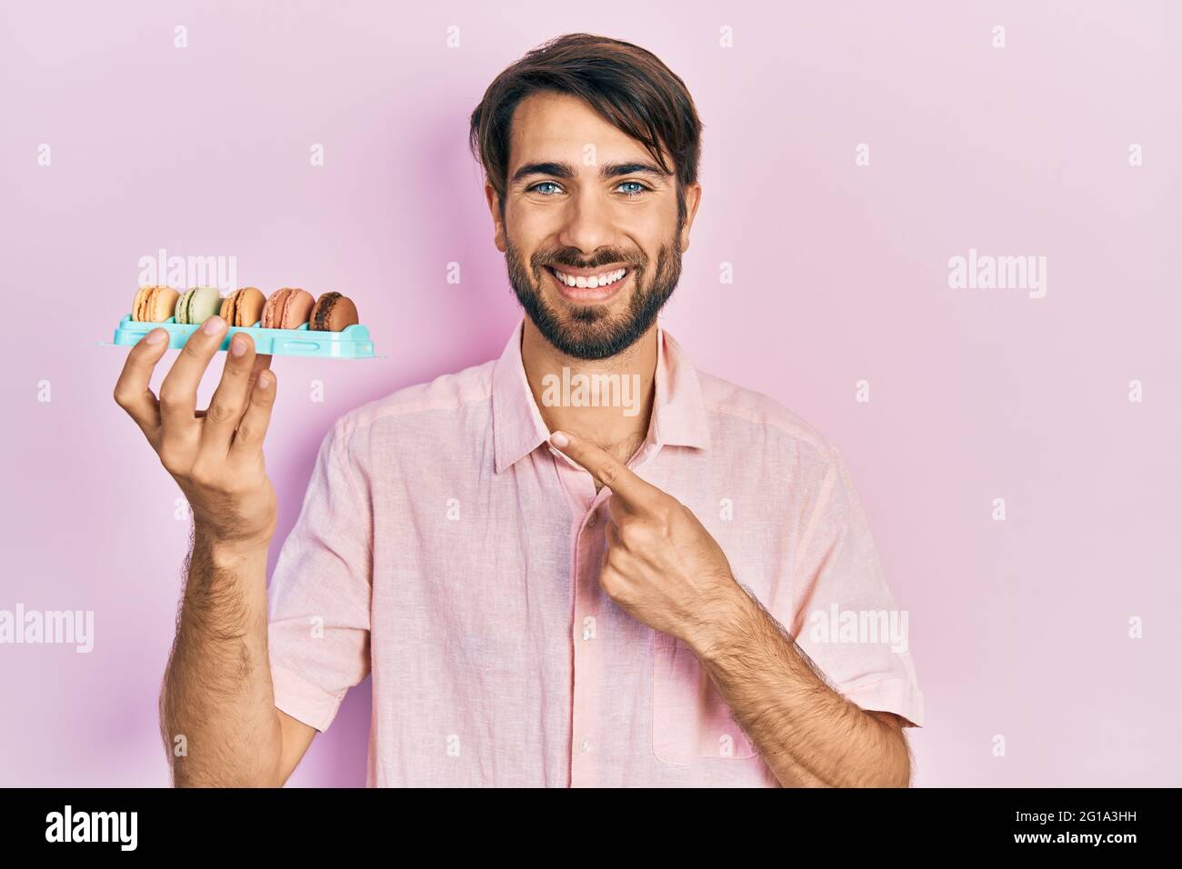 Jeune homme hispanique portant de délicieuses pâtisseries de macrons souriant, souriant, souriant, pointant avec la main et le doigt Banque D'Images