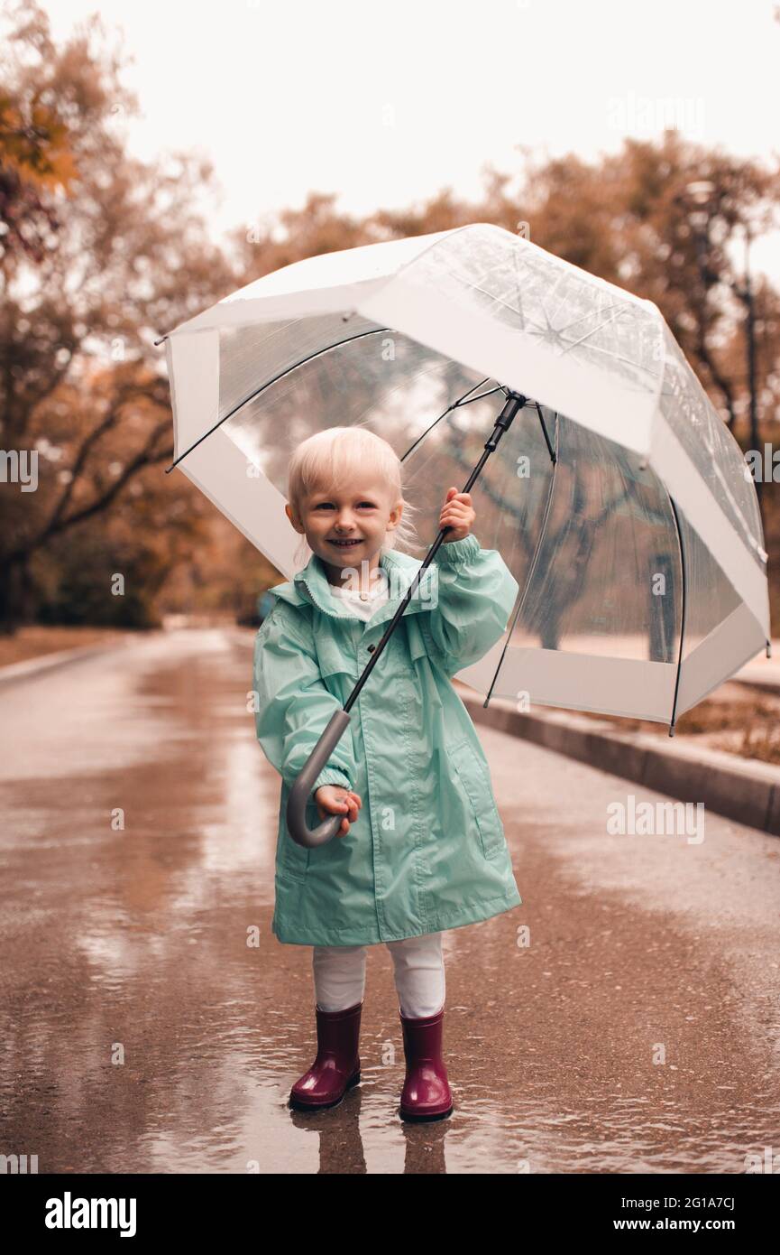 Joli petit enfant fille 4-5 ans tenir parapluie porter manteau de pluie et  bottes en caoutchouc dans le parc à l'extérieur. Regarder l'appareil photo.  Enfance. Concept de la saison d'été Photo Stock -