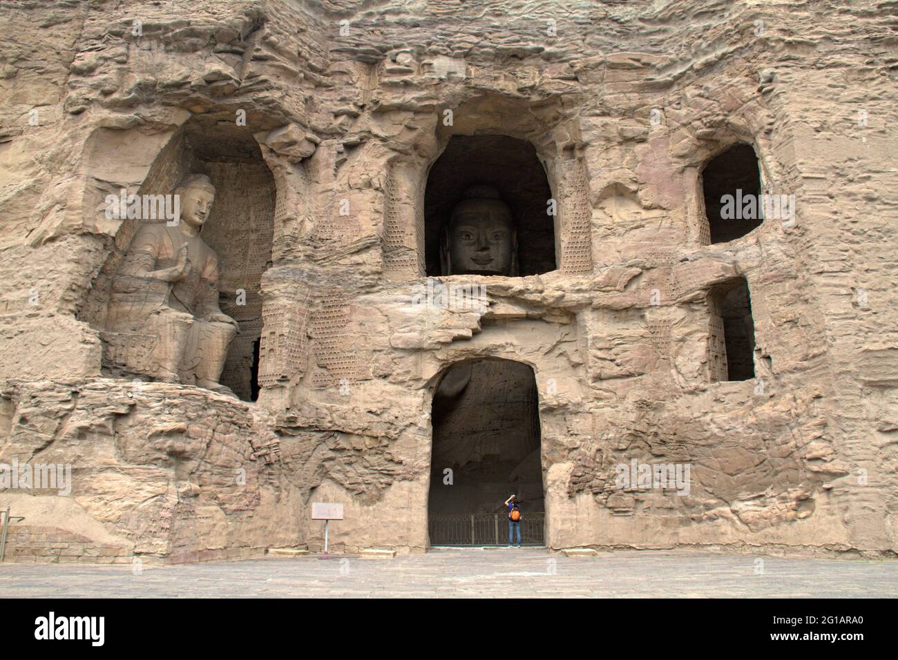 Des images anciennes de Bouddha sculptées dans des grottes de grès et des cavités dans la falaise de la grotte de Yungang près de Datong, Shanxi, Chine, nains un visiteur en contrebas. Banque D'Images